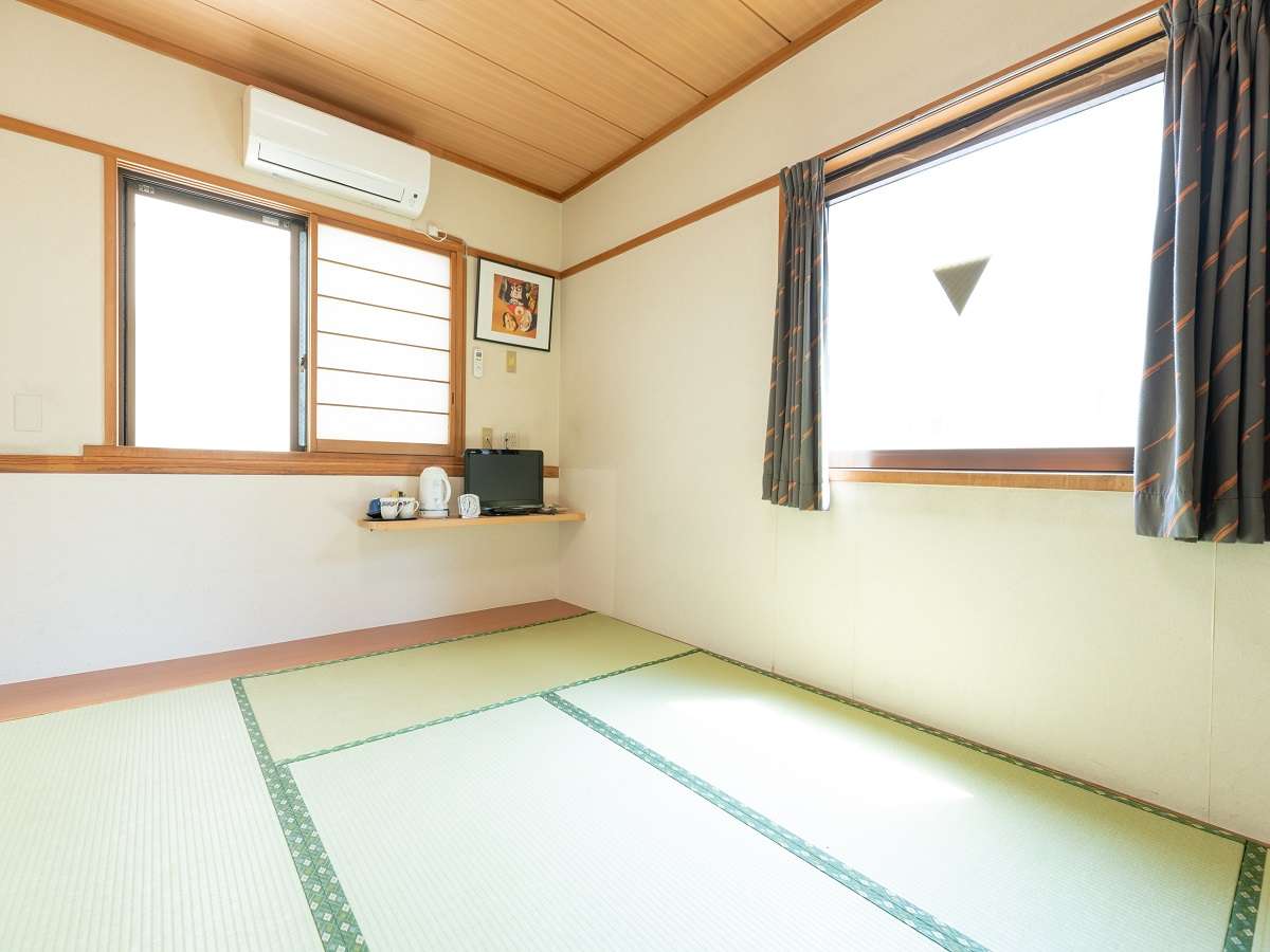 Sunlit tatami guest room at Sakura Ryokan with a large window, framed print and tea set
