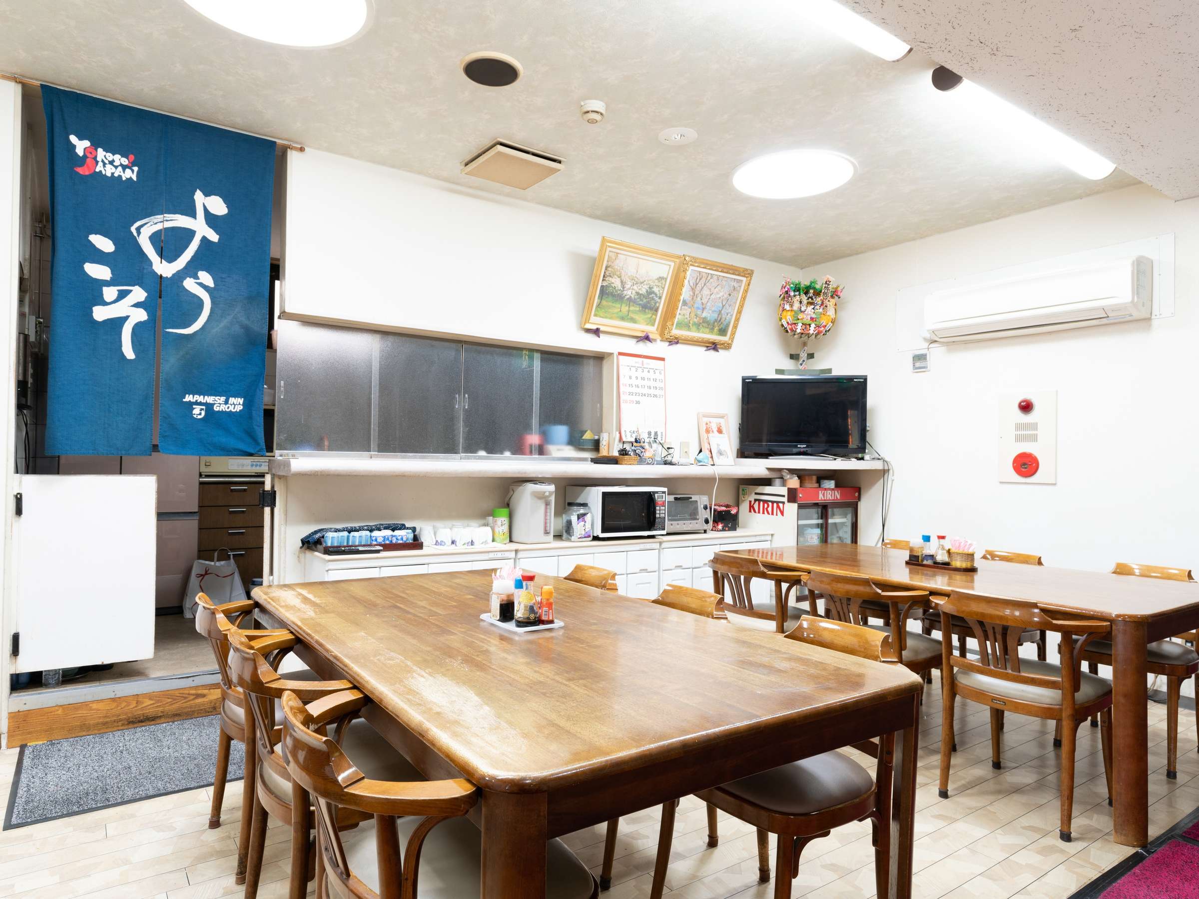 Communal dining room at Sakura Ryokan, Asakusa-Iriya, with wooden tables, chairs and a small kitchen counter