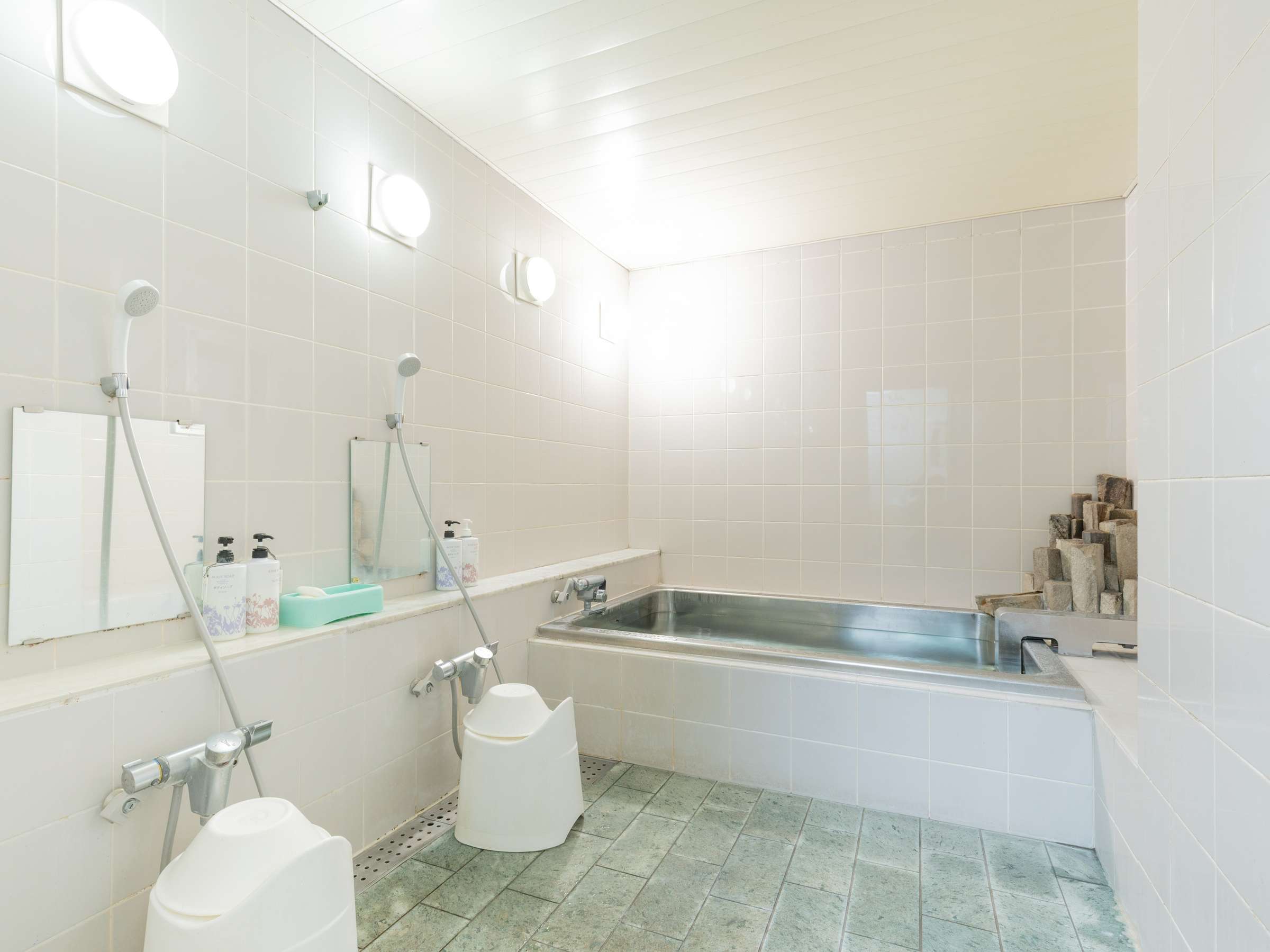 Bright tiled communal bath at Sakura Ryokan with a stainless steel soaking tub and shower stations