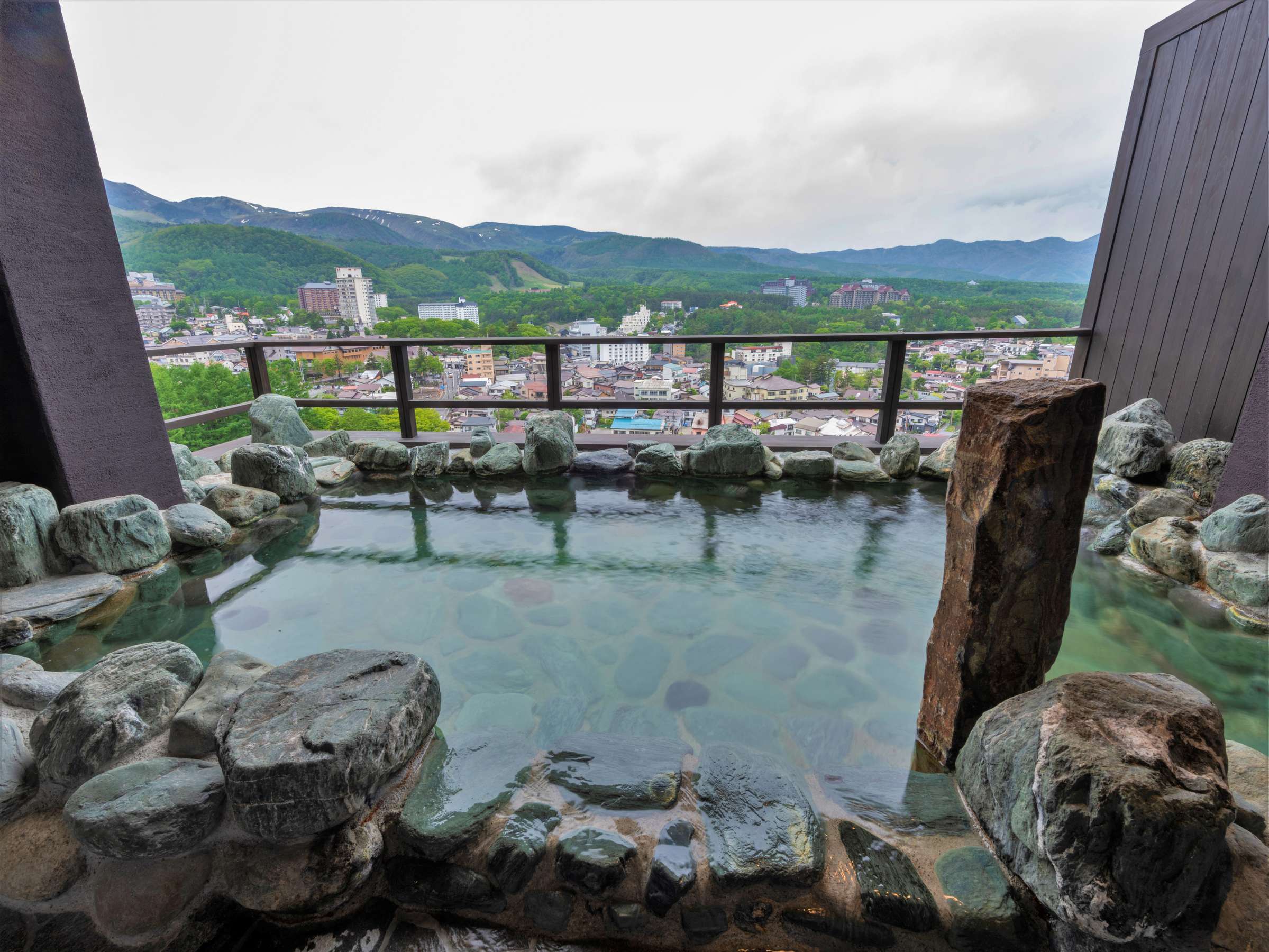 Rooftop rotenburo at La Vista Kusatsu Hills with green stone paving and a sweeping view over Kusatsu town in spring