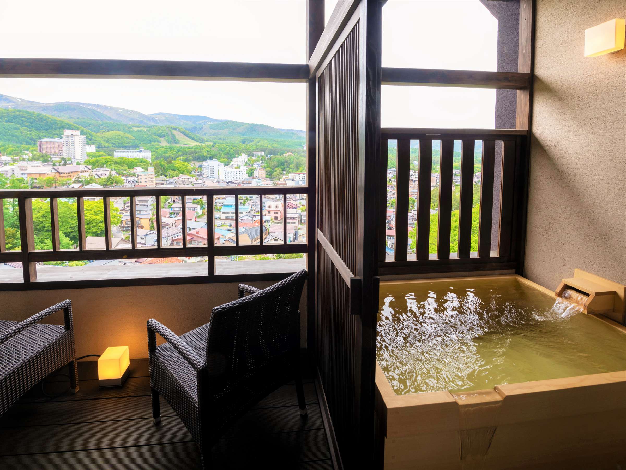 Guest-room private cypress-wood open-air bath at La Vista Kusatsu Hills filled with thermal water above a town and mountain view