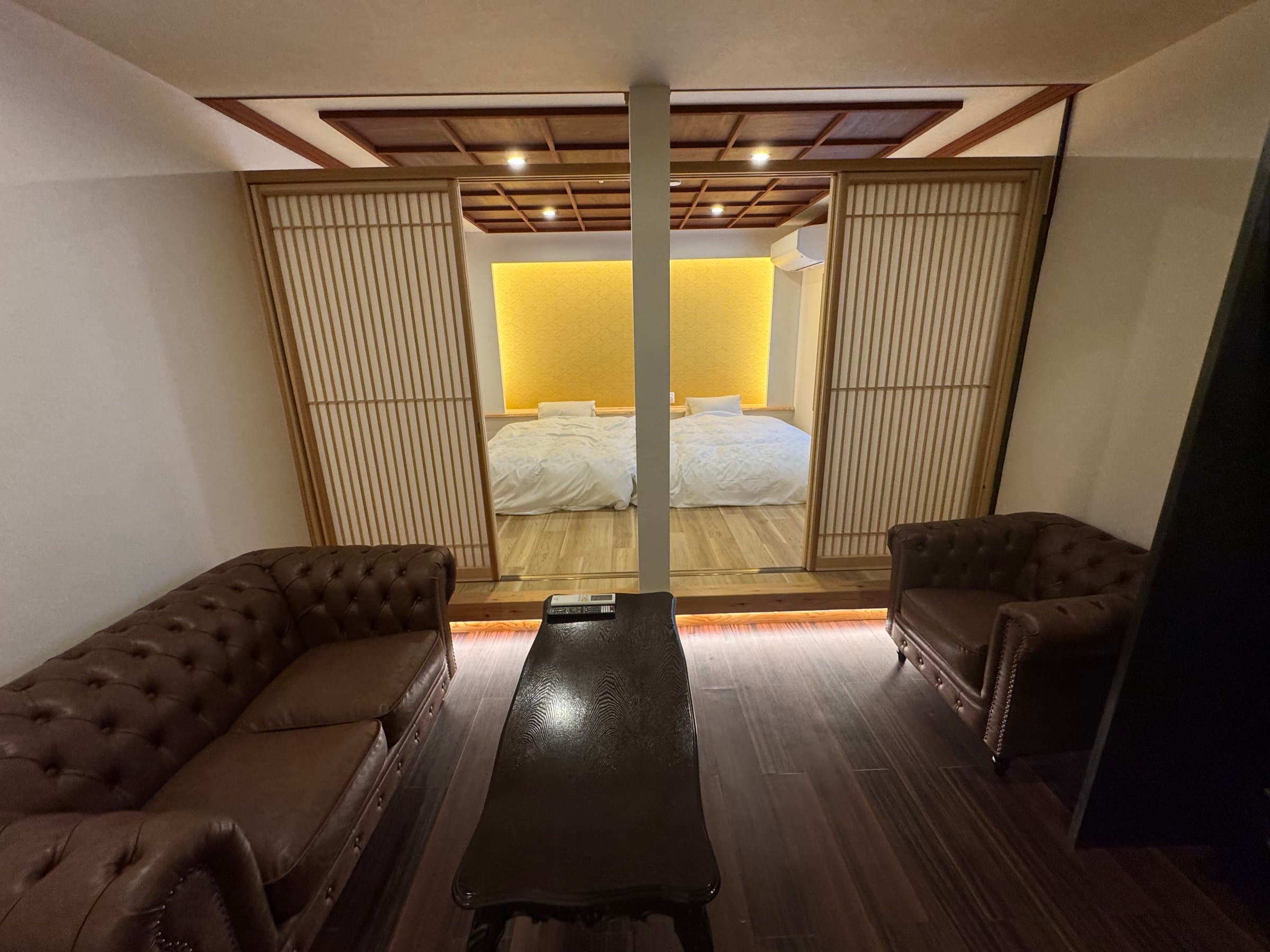 Suite lounge with antique leather sofas and a bedroom behind shoji sliding screens at Oyado Yanadaya