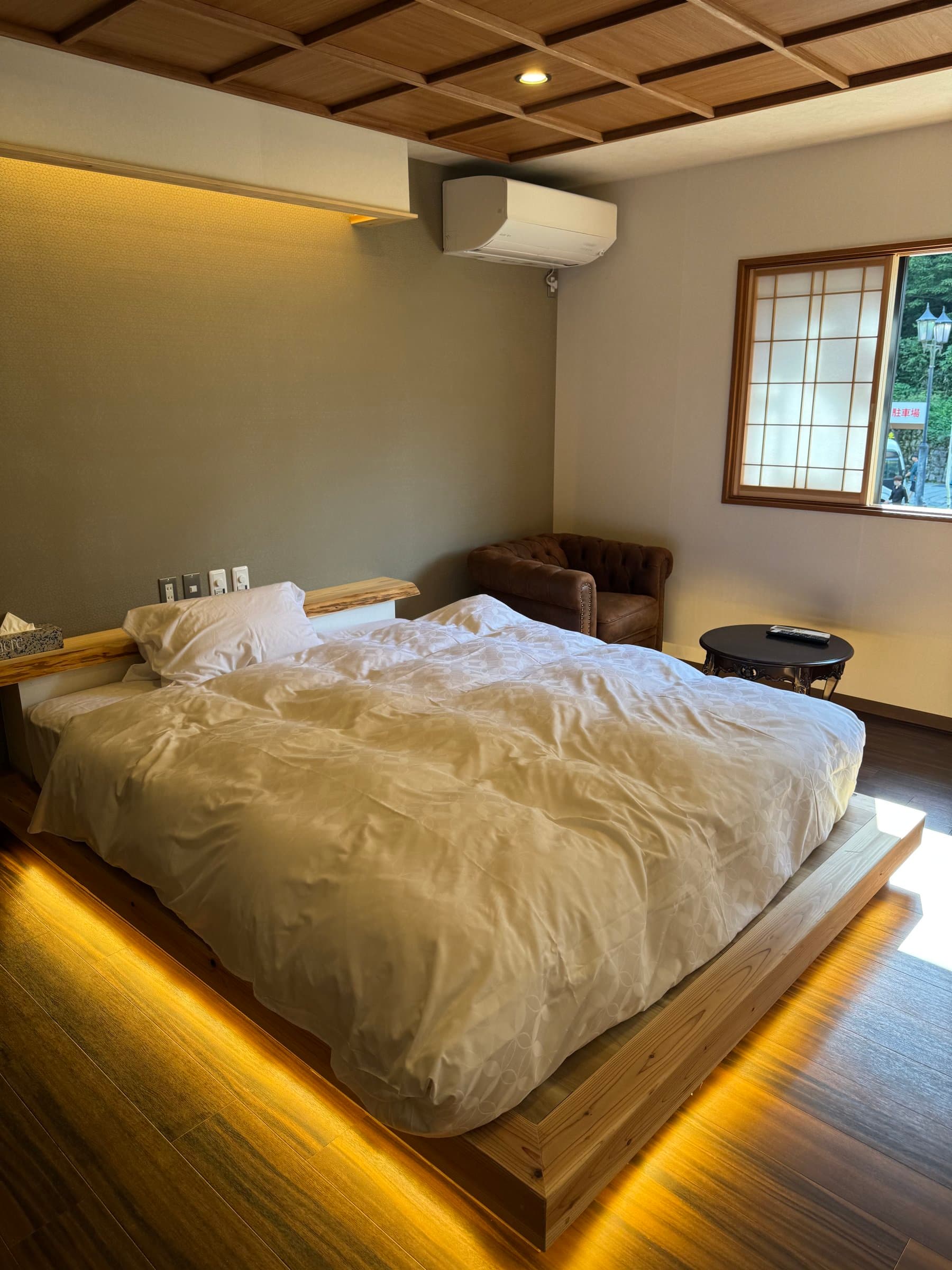 Guest room with a king bed on an illuminated wooden platform and a latticed window at Oyado Yanadaya in Ginzan Onsen