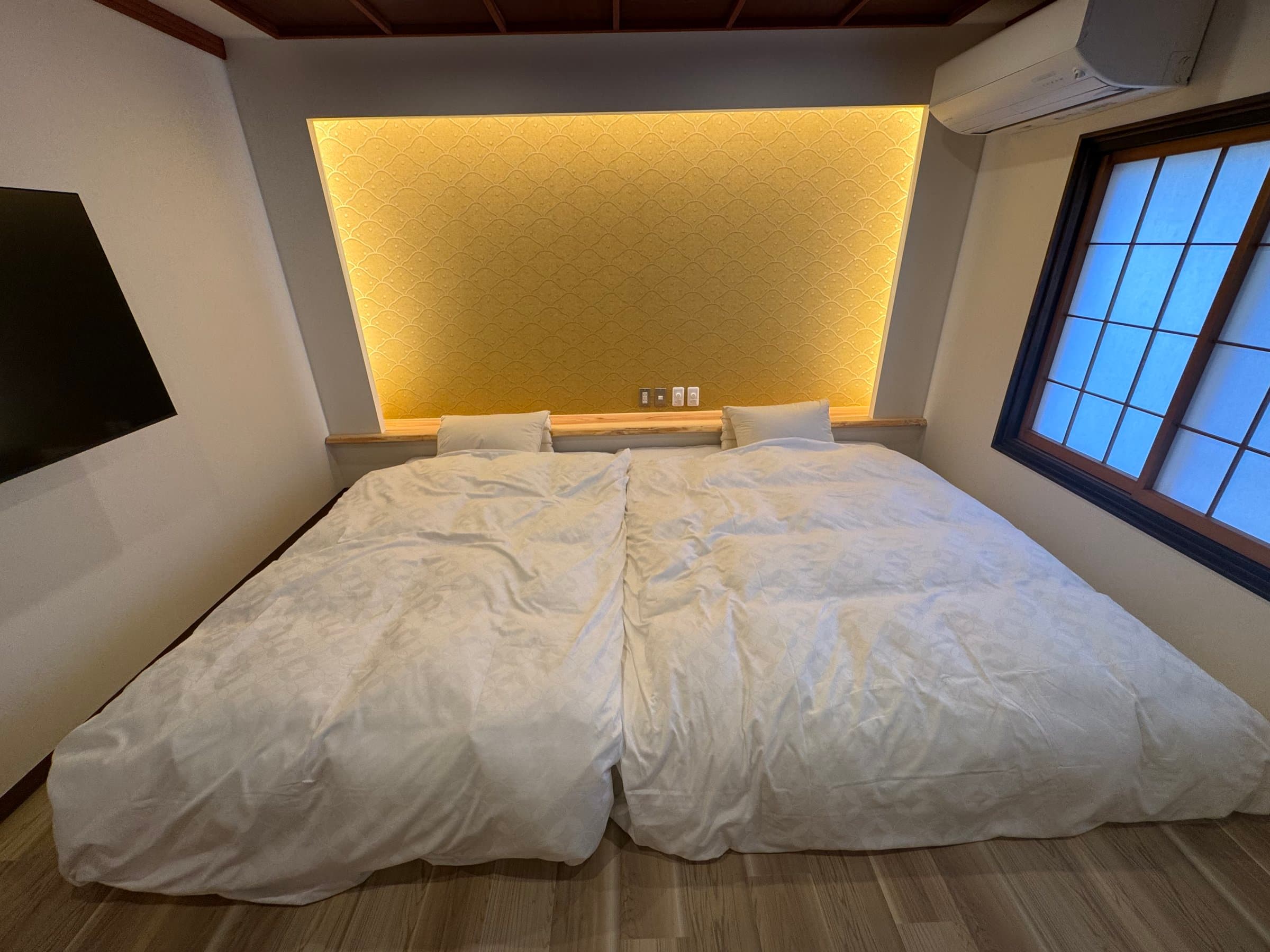 Twin-bed guest room with a softly lit washi headboard and shoji window at Yanadaya in Ginzan Onsen