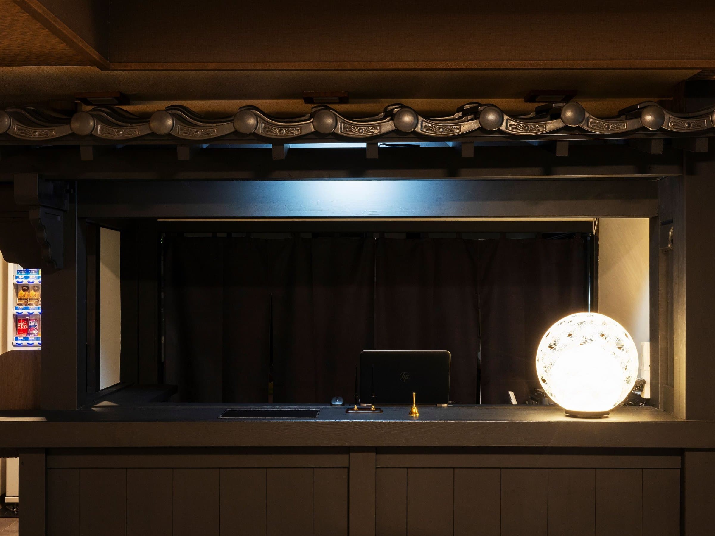 Yusai Bekkan front desk with dark timber counter, decorative tiled cresting and a glowing spherical lantern