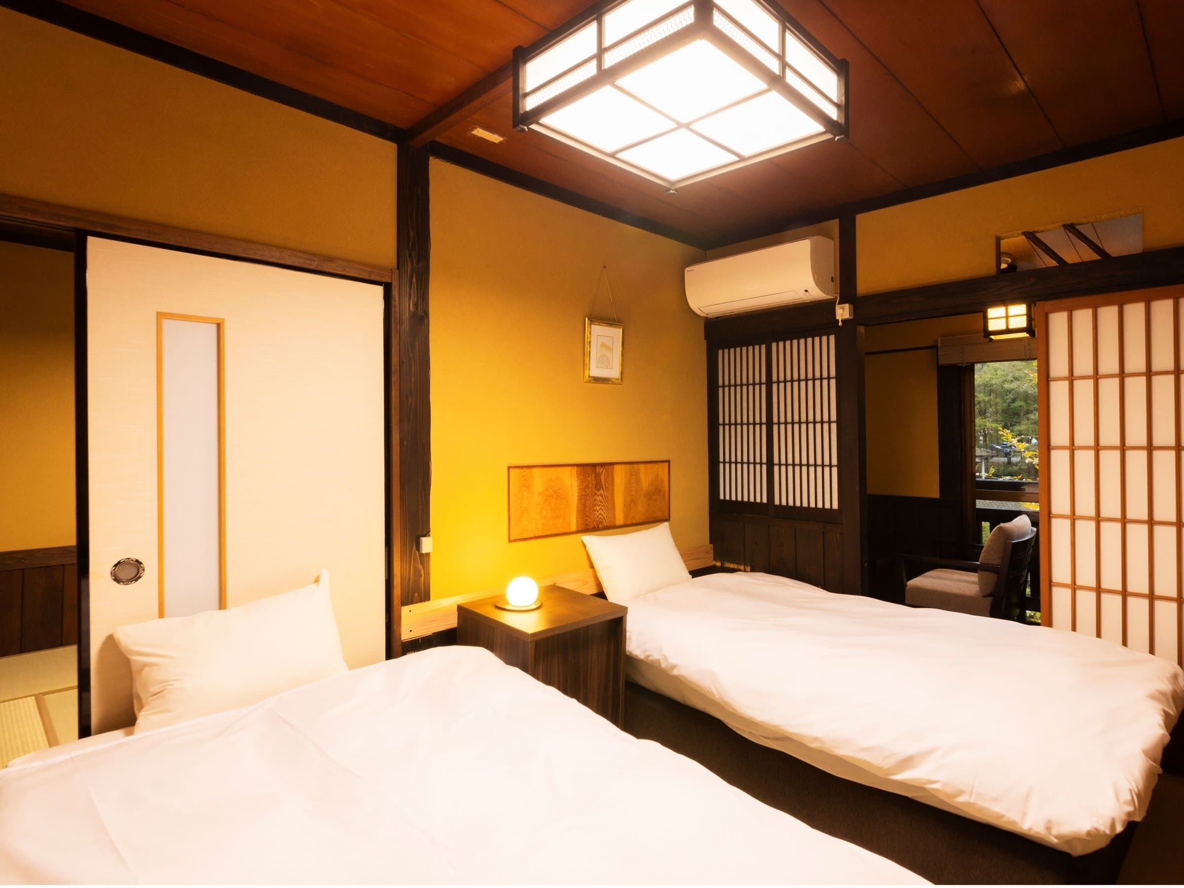Twin-bed Japanese-style guest room at Yusai Bekkan with tatami floor, ochre walls and shoji screens overlooking greenery