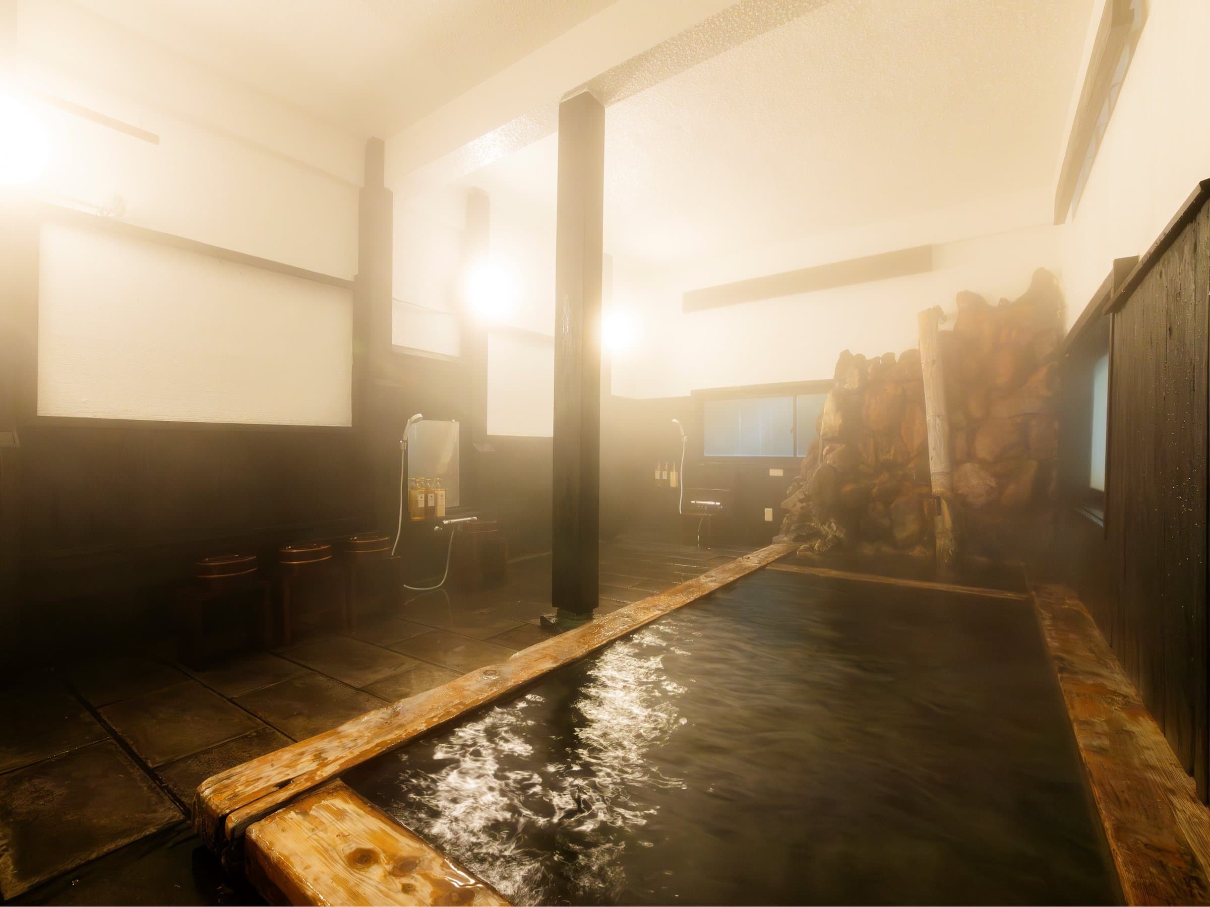 Steamy indoor onsen bath at Yusai Bekkan, long stone-walled pool with timber posts and washing stations