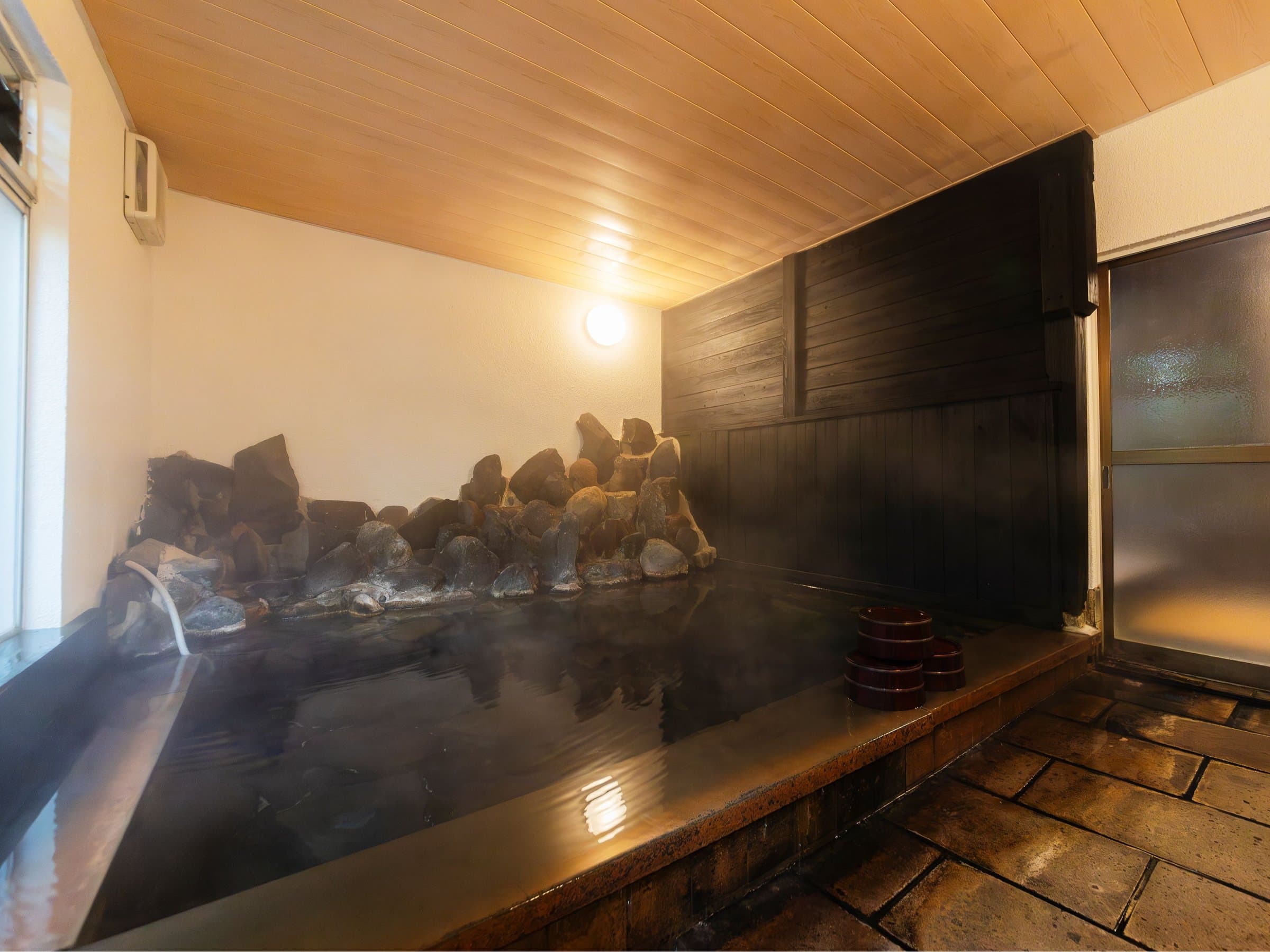 Stone-rimmed indoor onsen bath at Yusai Bekkan with rock edging and wooden ceiling