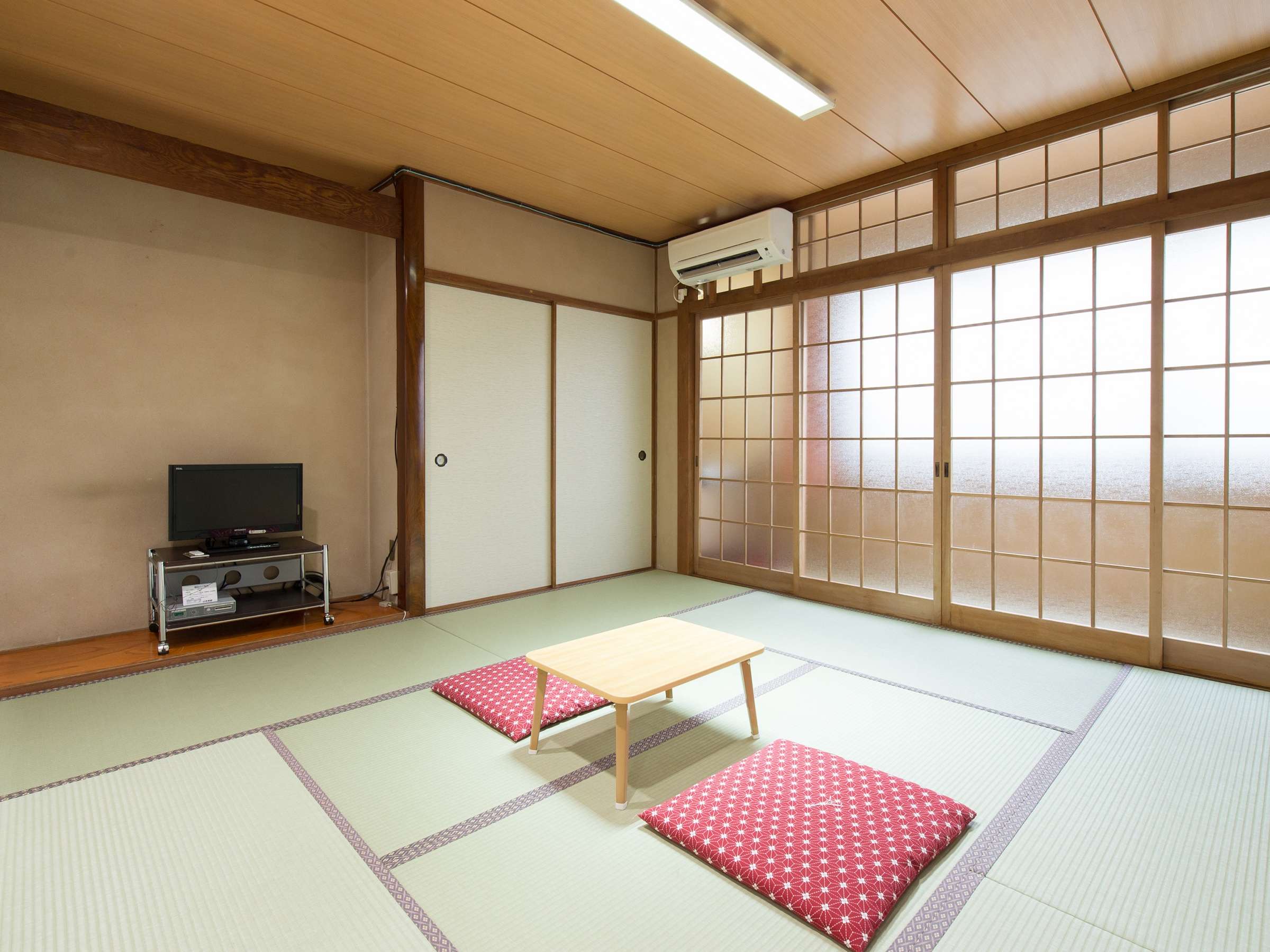 Bright Japanese-style tatami guest room with sliding shoji screens, floor cushions and a flat-screen TV at Yamamoto Ryokan