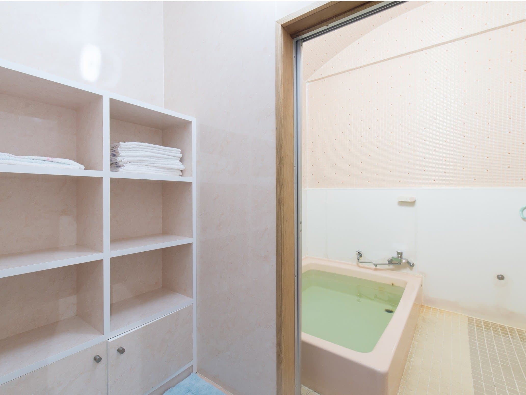Shared bath at Yamamoto Ryokan with a soaking tub viewed through a glass door and folded towels on open shelving