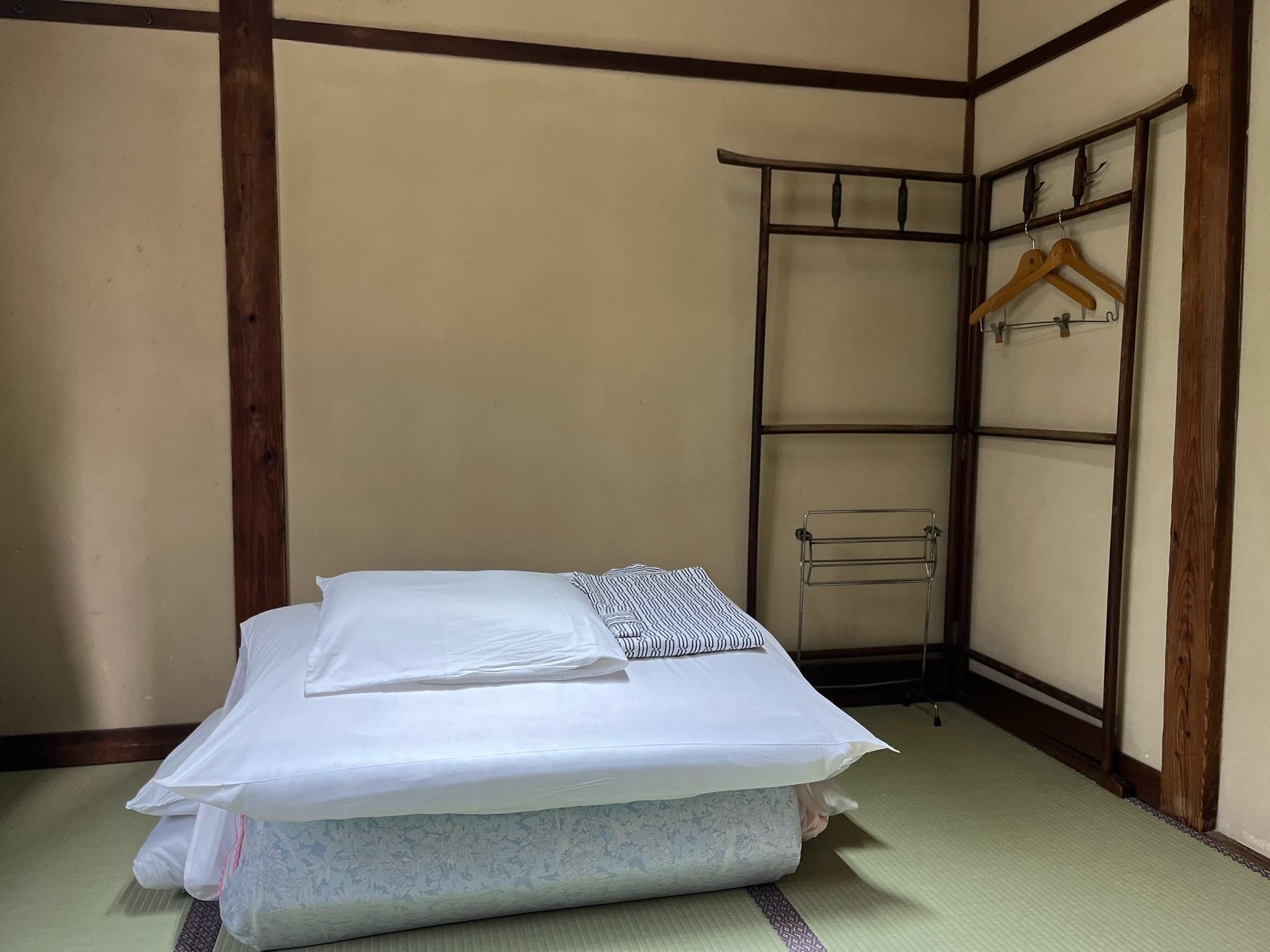 Tatami room with a freshly made white futon laid out and a wooden clothing rack at Yamamoto Ryokan