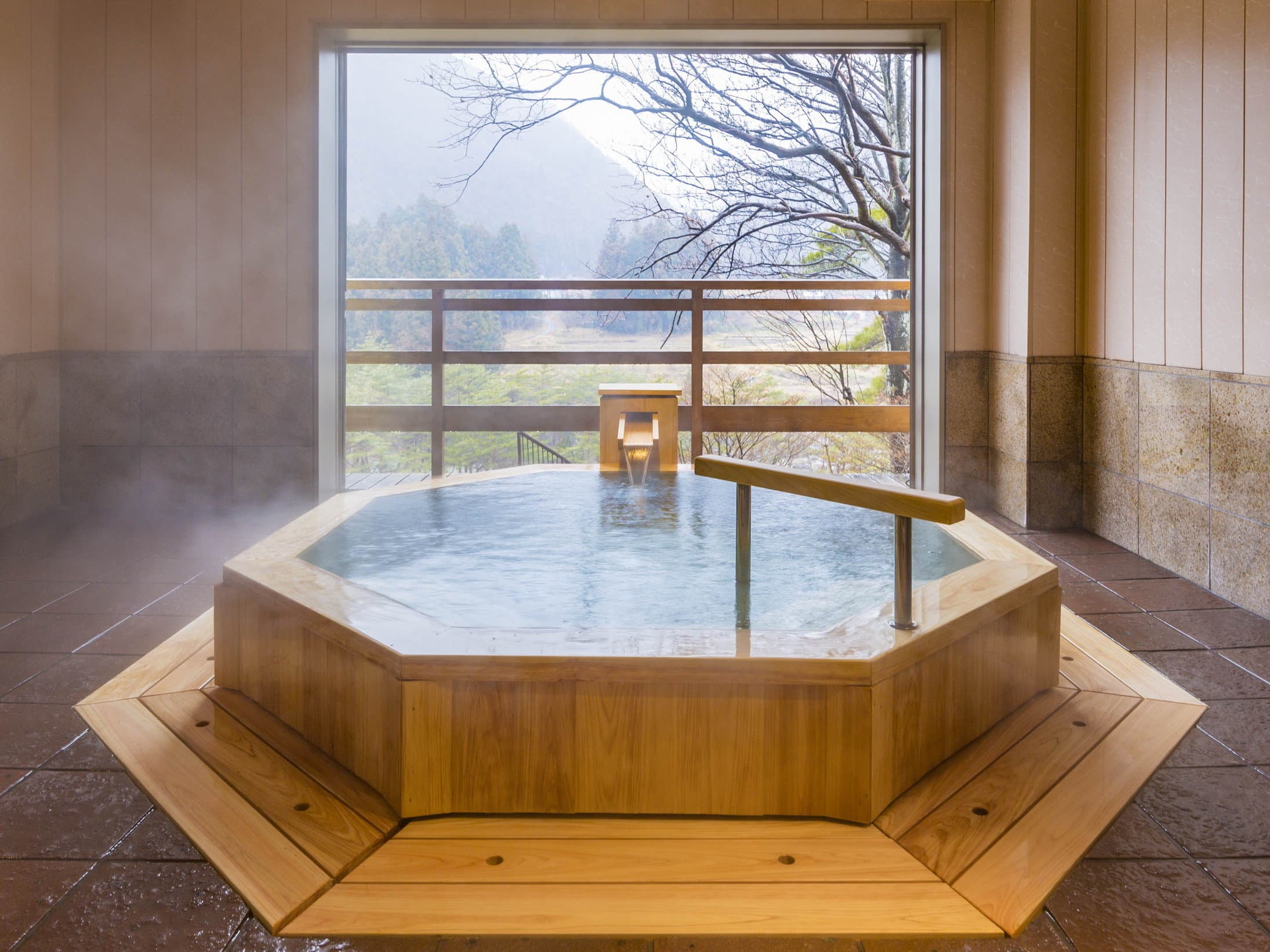 Indoor wooden octagonal hinoki hot spring bath steaming before a large window with mountain view at Wakatake no Sho, Nikko