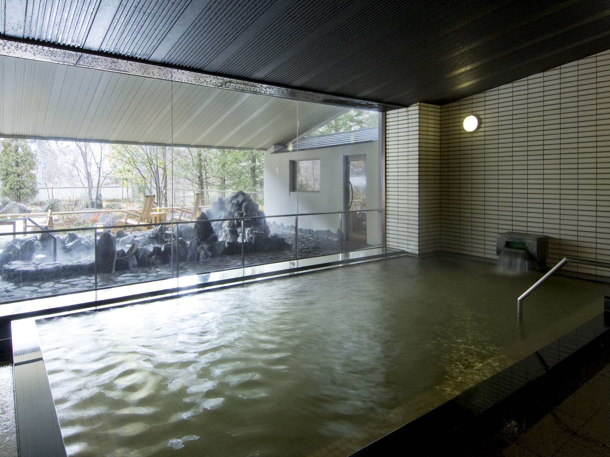 Indoor hot spring bath with tiled walls and large glass wall framing the garden at Nikko Senhime Monogatari