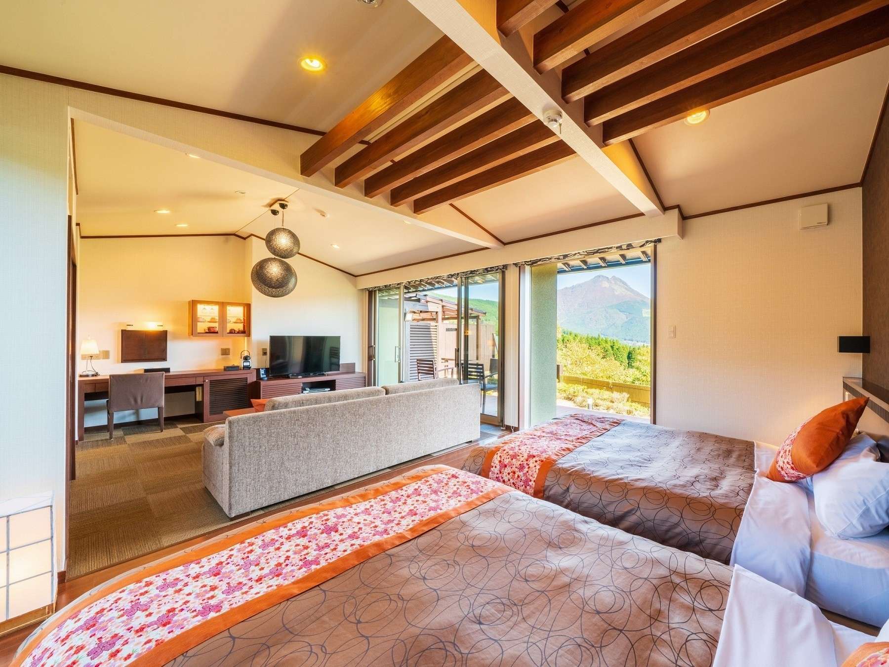 Spacious guest room at Yufuin Hanayoshi with twin beds, lounge seating and exposed beams framing a Mount Yufu view
