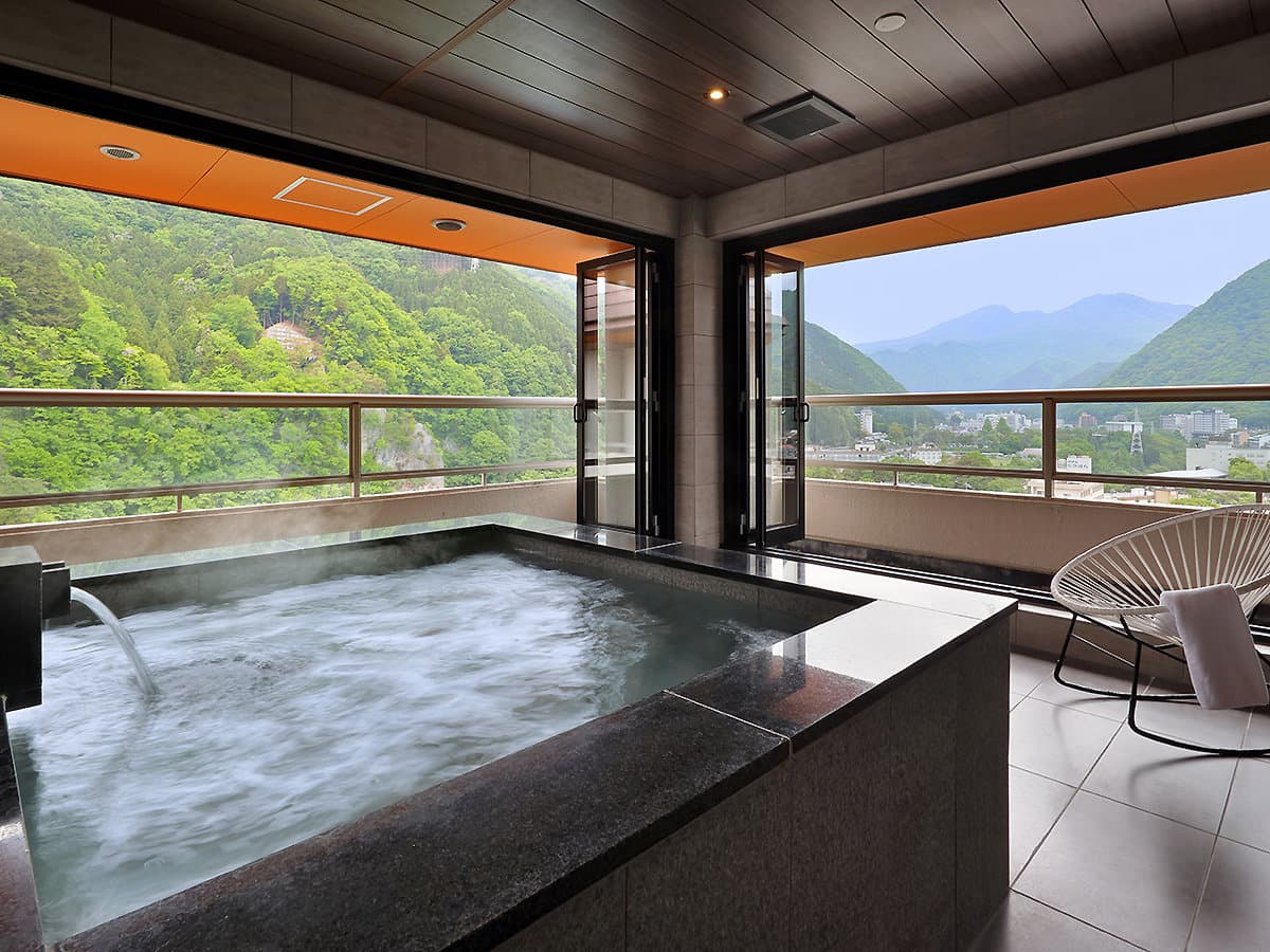 Indoor hot spring bath with picture windows overlooking the green Kinugawa gorge at Hotel Sunshine Kinugawa, Nikko