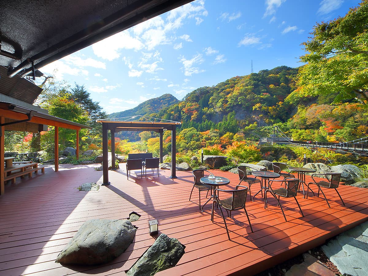 Open-air wooden terrace lounge with seating and pergola overlooking the autumn Kinugawa gorge at Hotel Sunshine Kinugawa