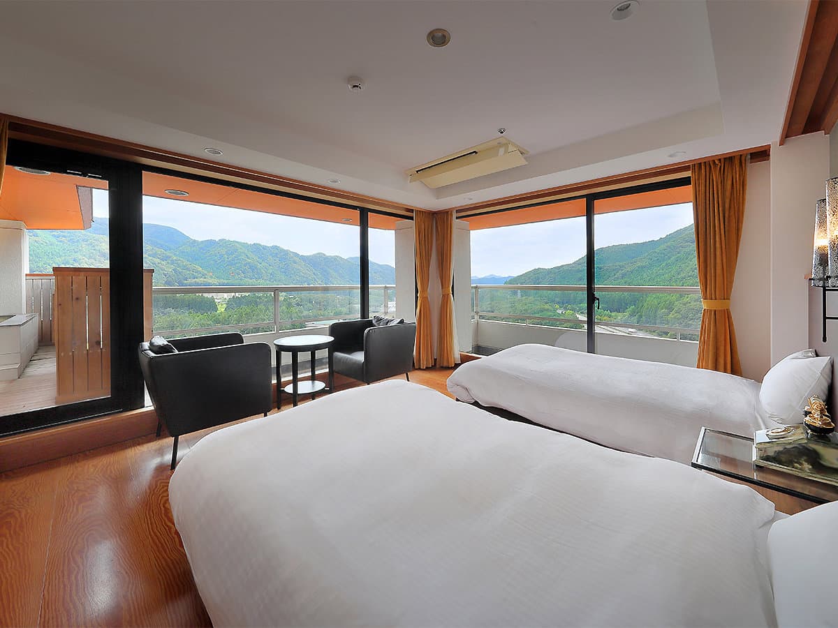 Bright Western-style guest room with twin beds and large windows framing the Kinugawa River valley at Hotel Sunshine Kinugawa