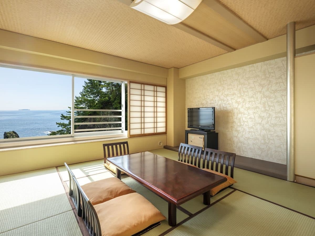 Tatami guest room with low table and floor cushions facing an ocean view at Hotel New Akao, Atami