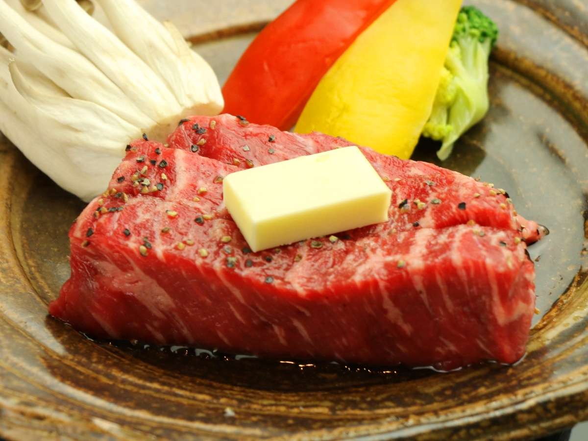 Close-up of a marbled wagyu beef steak topped with butter beside grilled vegetables on a rustic plate