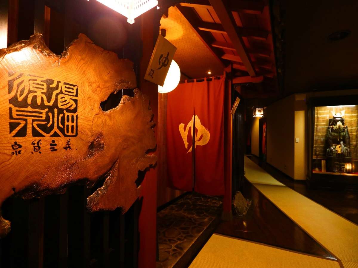 Atmospheric interior bath entrance with a carved wooden plaque and a red noren curtain over a stone-floored passage
