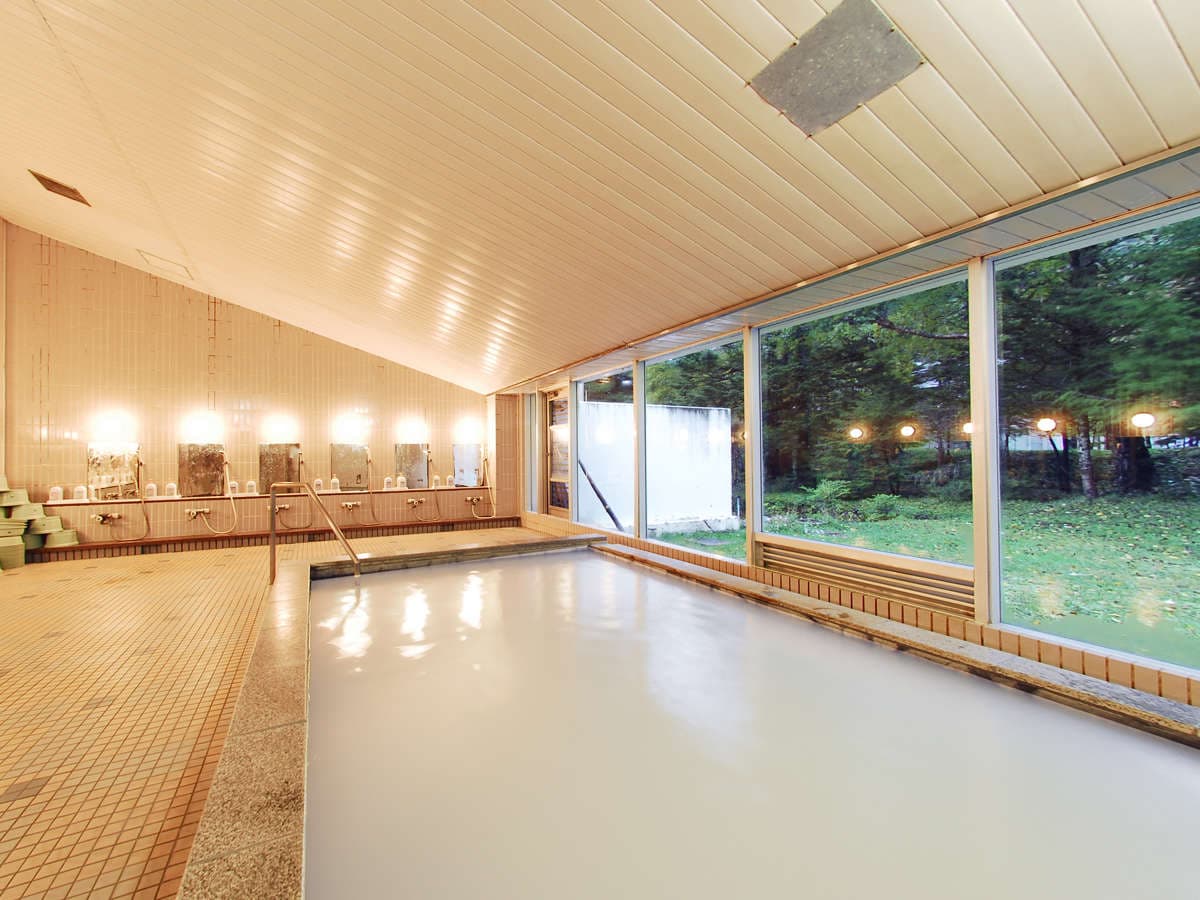 Indoor sulfur hot spring bath with milky white water and large windows facing the forest at Okunikko Kogen Hotel
