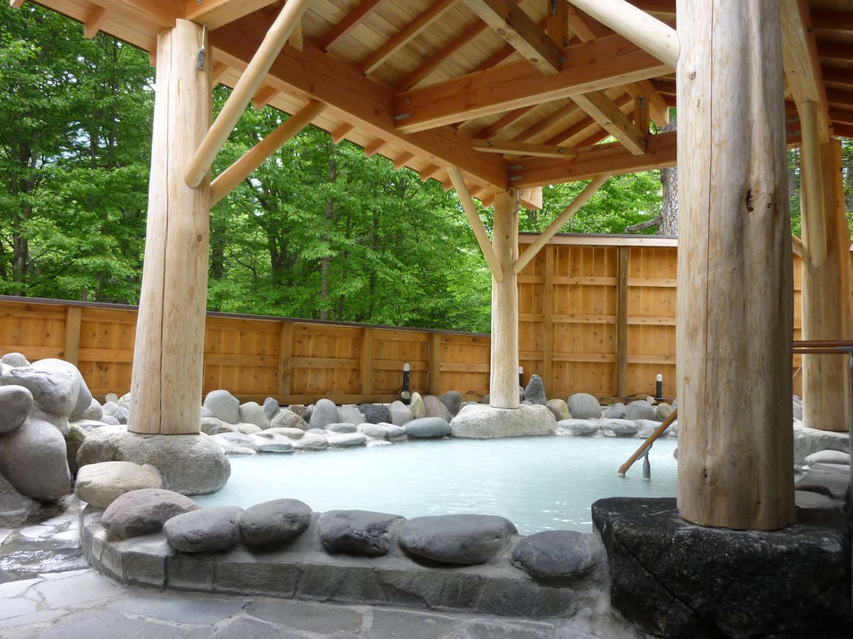 Outdoor rotenburo hot spring with milky sulfur water under a log pavilion surrounded by summer greenery at Okunikko Kogen Hotel