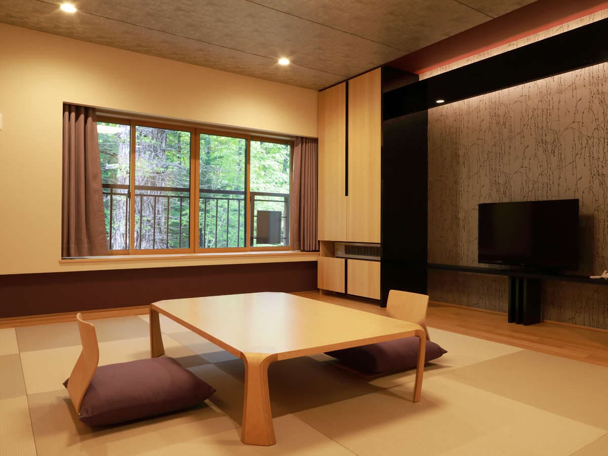 Spacious modern Japanese guest room with low table, zaisu chairs and forest-view window at Okunikko Kogen Hotel
