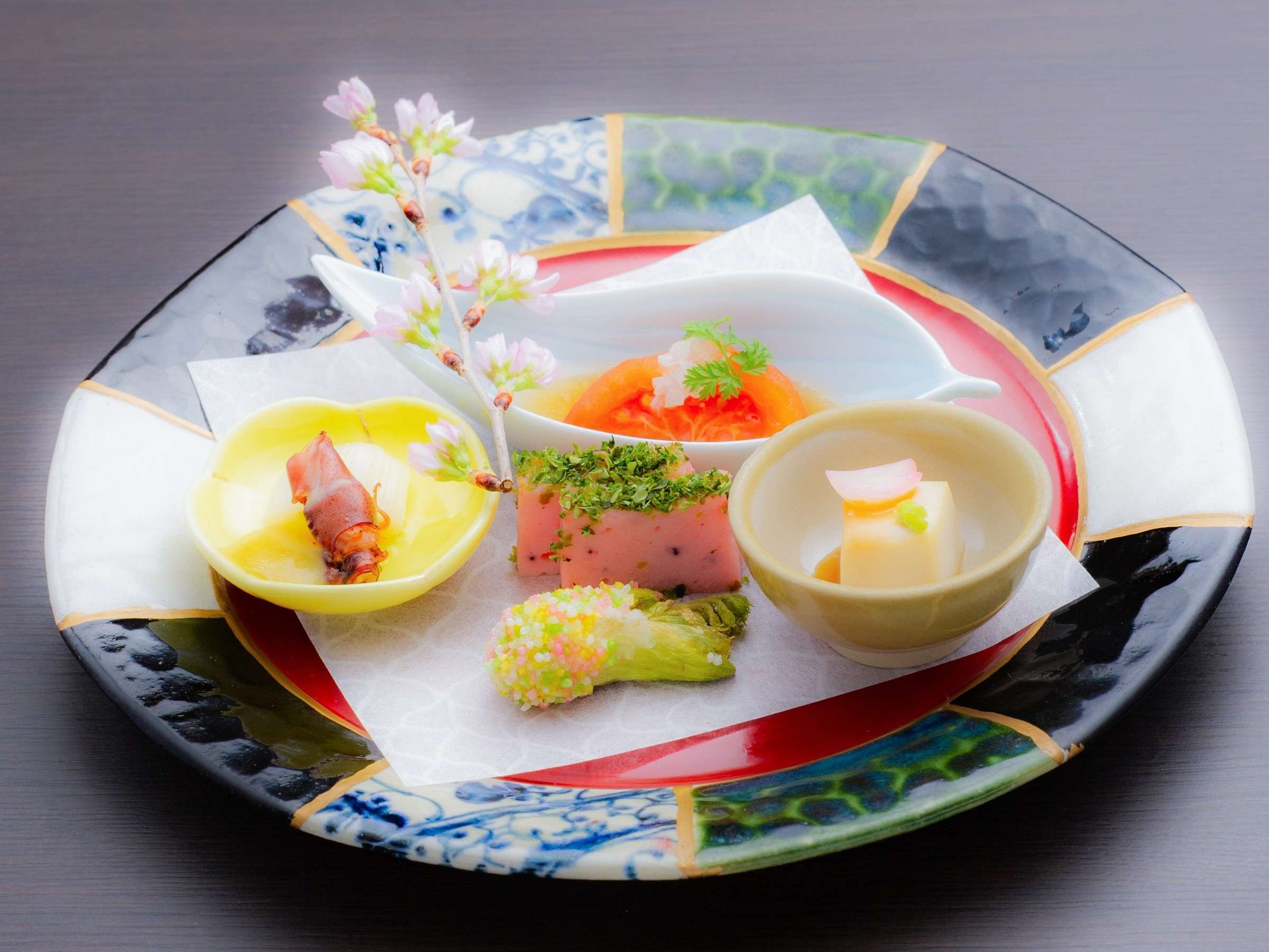 Kaiseki appetizer plate with seasonal delicacies and cherry-blossom garnish on a hand-painted dish at Okunikko Kogen Hotel