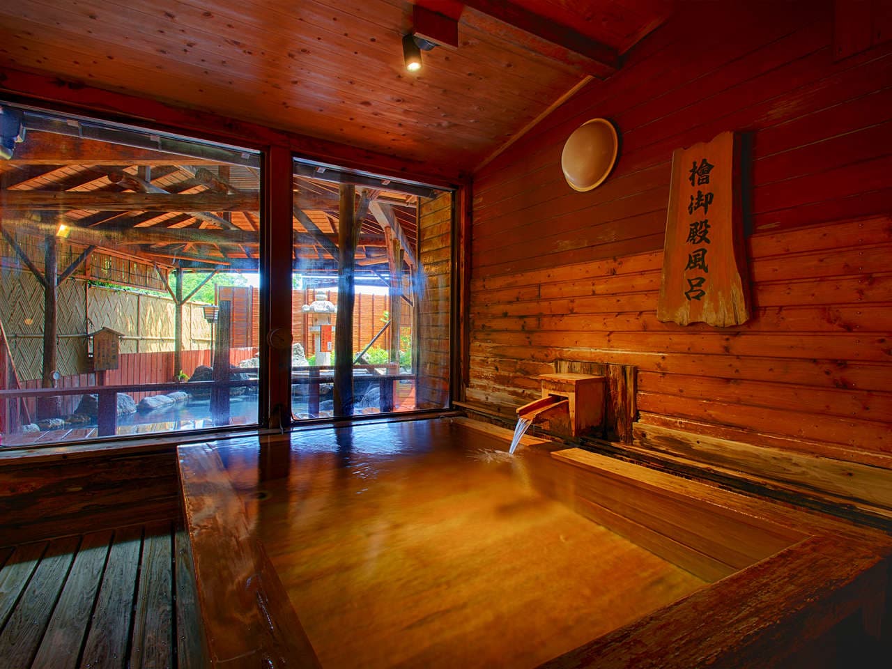 Indoor hinoki cypress soaking bath with hot spring water flowing from a wooden spout at Atagawa Prince Hotel