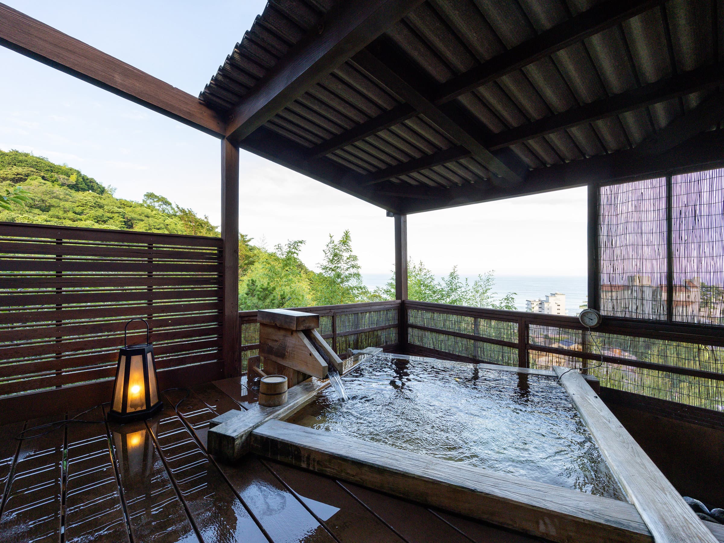 Private wooden rotenburo bath with a stone lantern and ocean-view deck at dusk, Atagawa Onsen, Izu