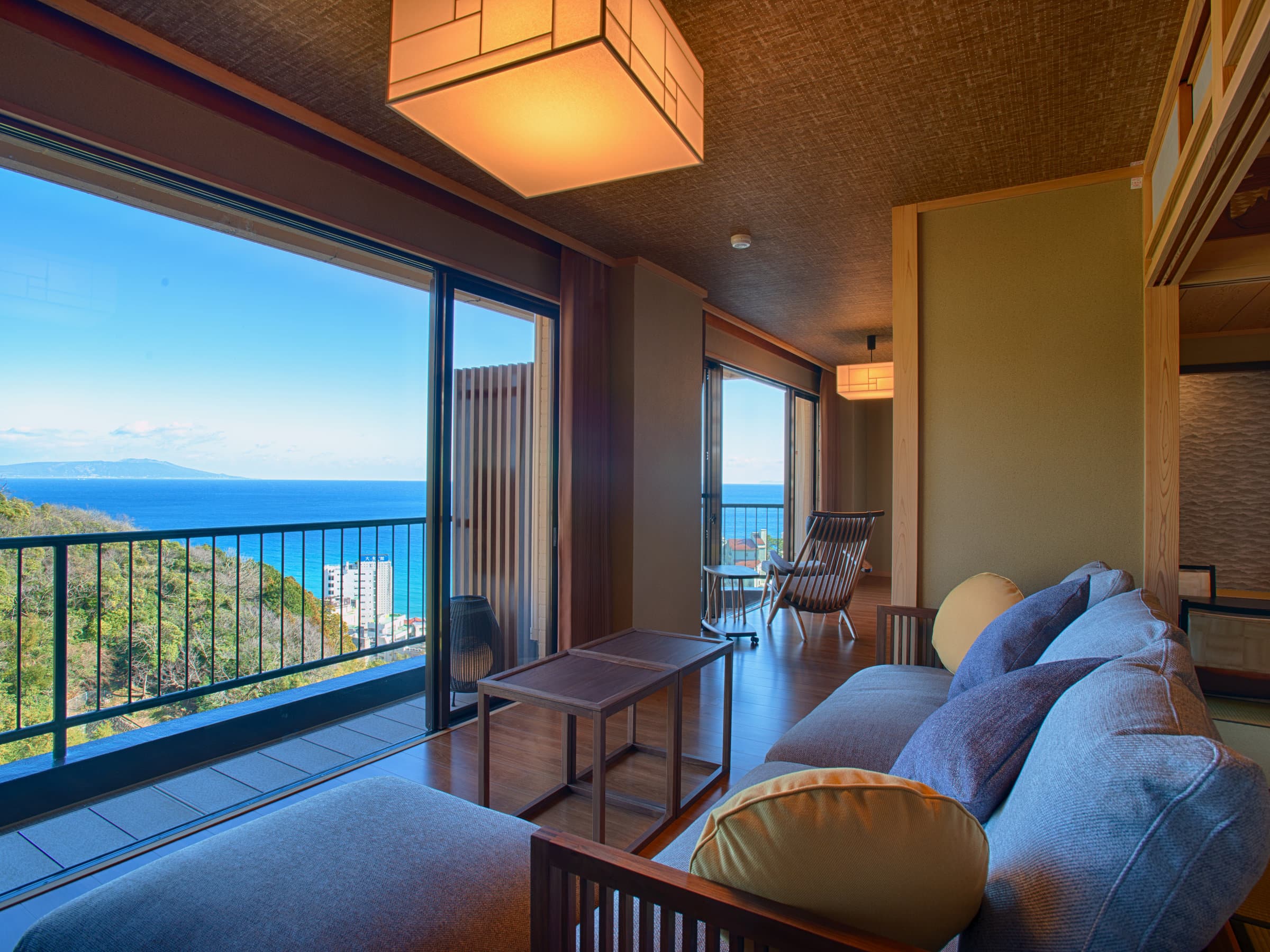 Tatami-trimmed guest room lounge with sofa and floor-to-ceiling windows framing the Sagami Bay ocean view, Atagawa Onsen
