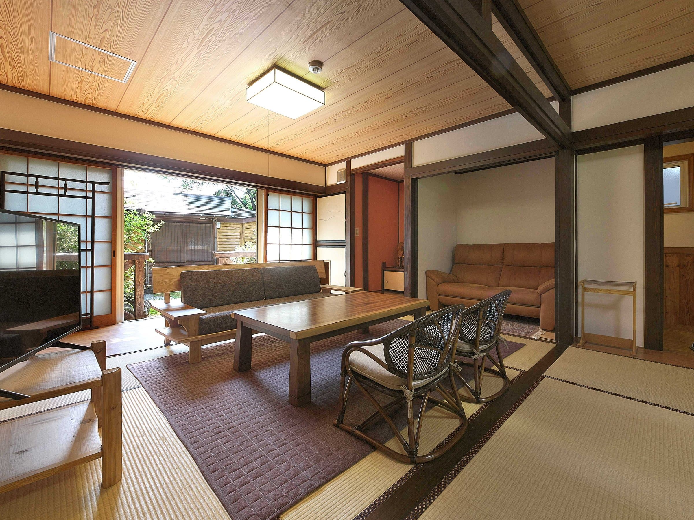 Spacious tatami guest room with a low wooden table, leather sofa and shoji windows facing a garden