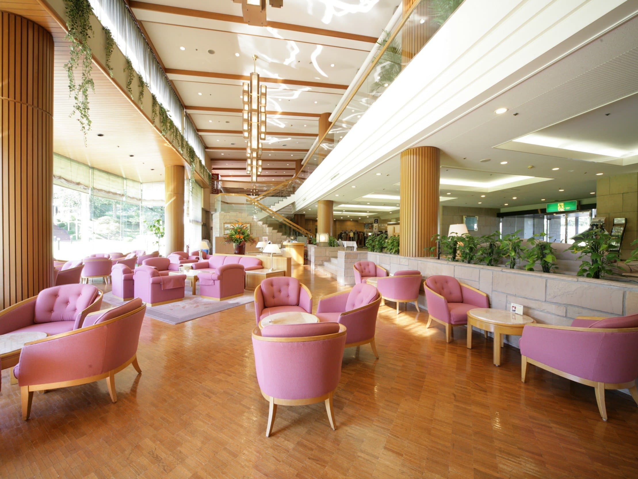 Bright hotel lobby lounge with pink armchairs and greenery