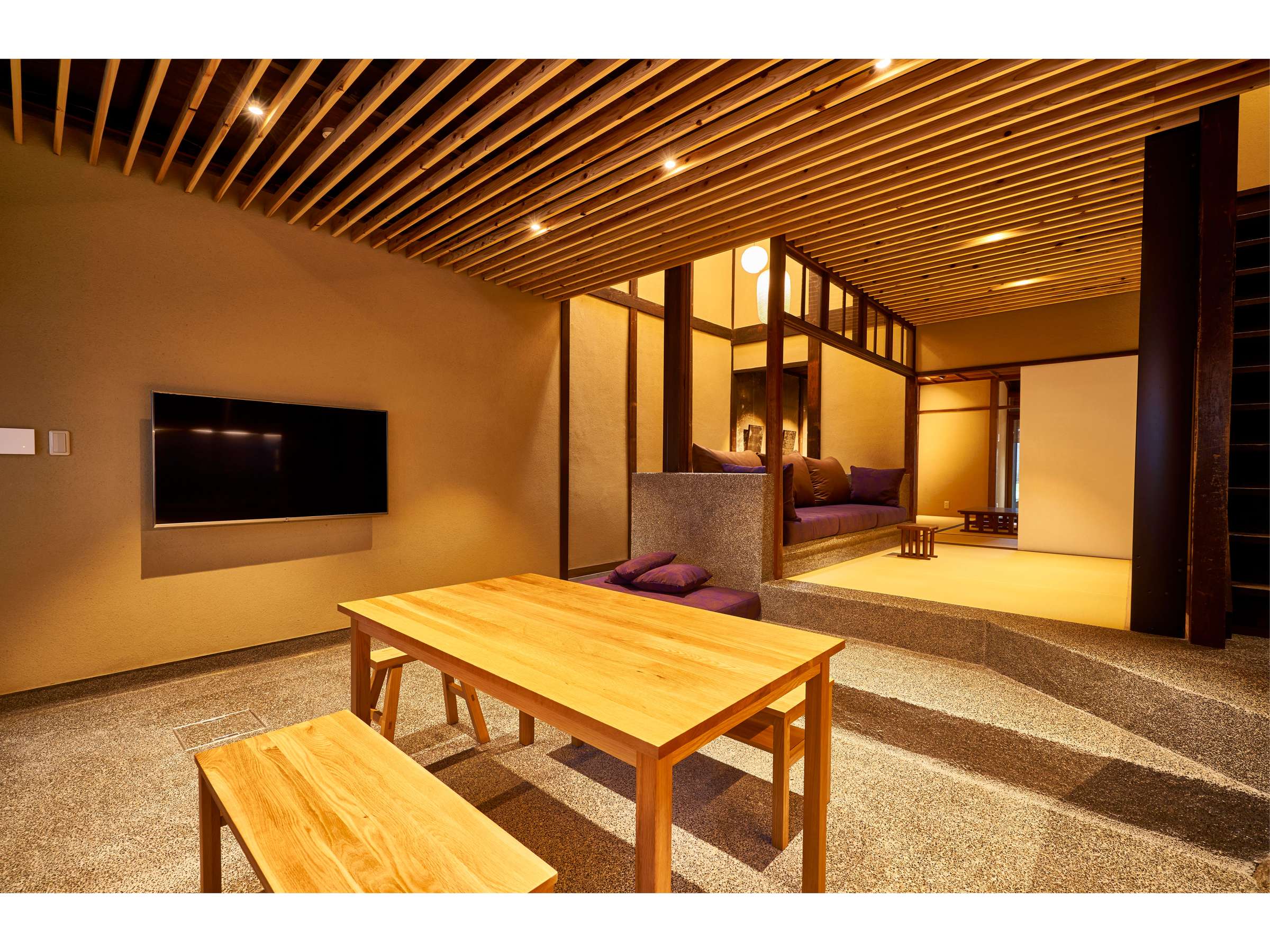 Living and dining lounge at Zen-Oyado Nishitei with a wooden table, slatted ceiling and a raised tatami sitting area beyond