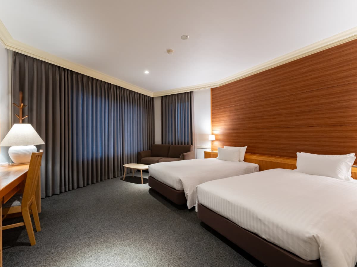 Spacious twin guest room with desk and lounge sofa and warm wood headboard at Hotel Sierra Resort Hakuba