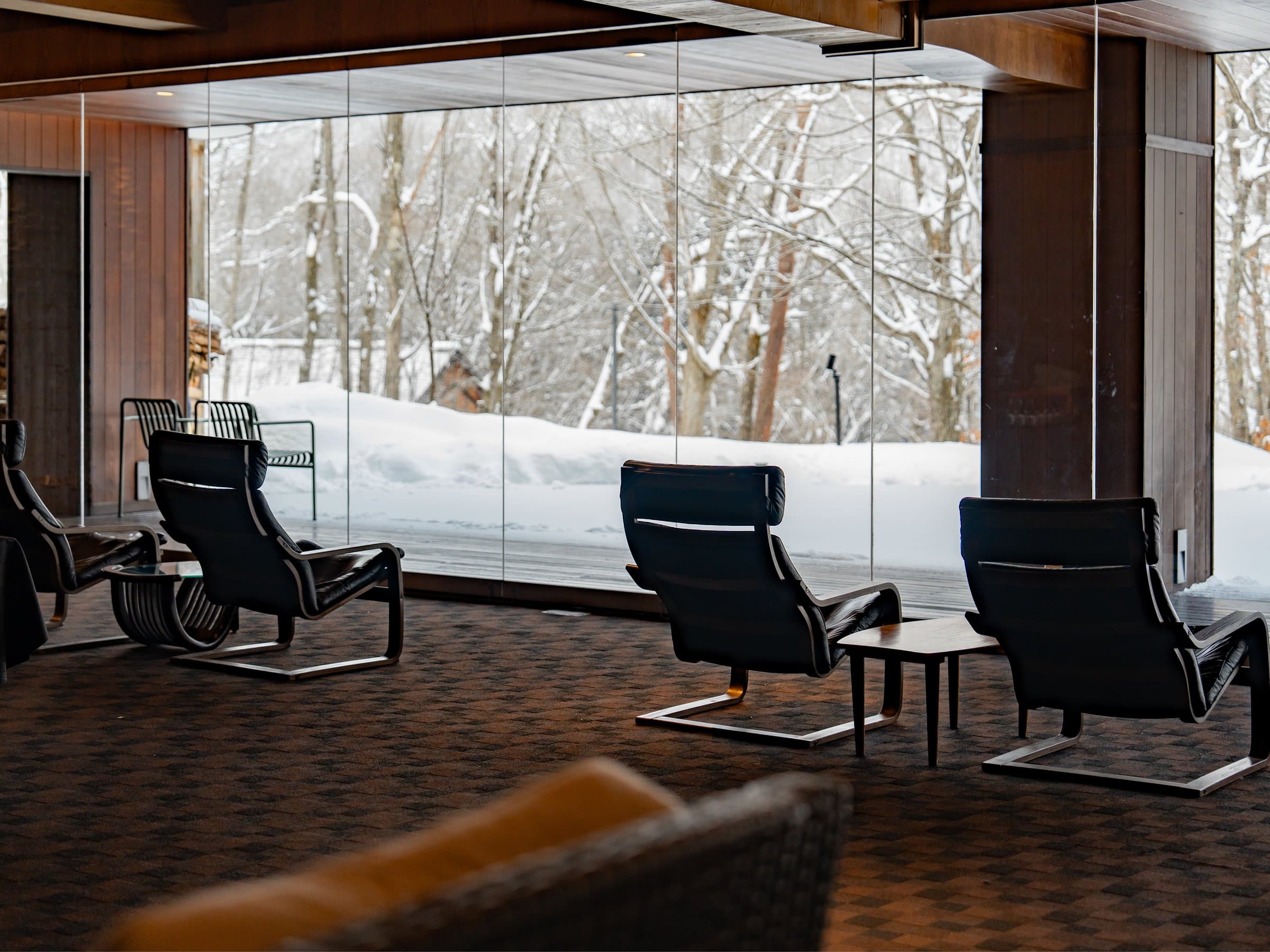 Lounge with leather armchairs facing floor-to-ceiling glass and a snowy forest view at Hotel Sierra Resort Hakuba
