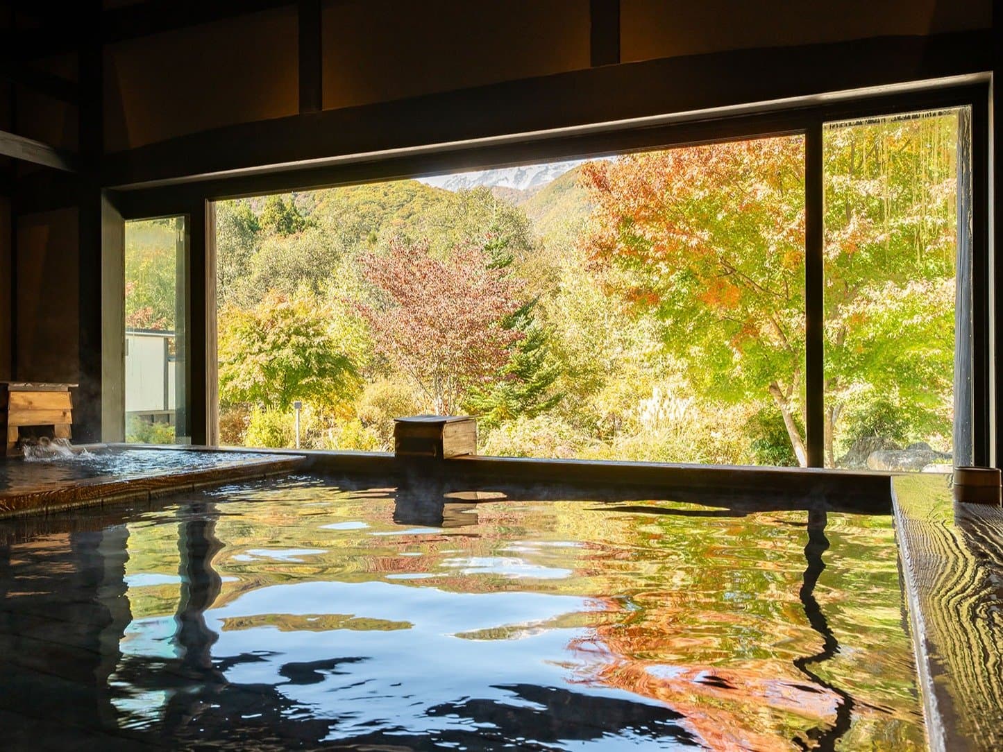 Indoor hot-spring bath at Hotel Sierra Resort Hakuba with a wide window framing autumn mountains
