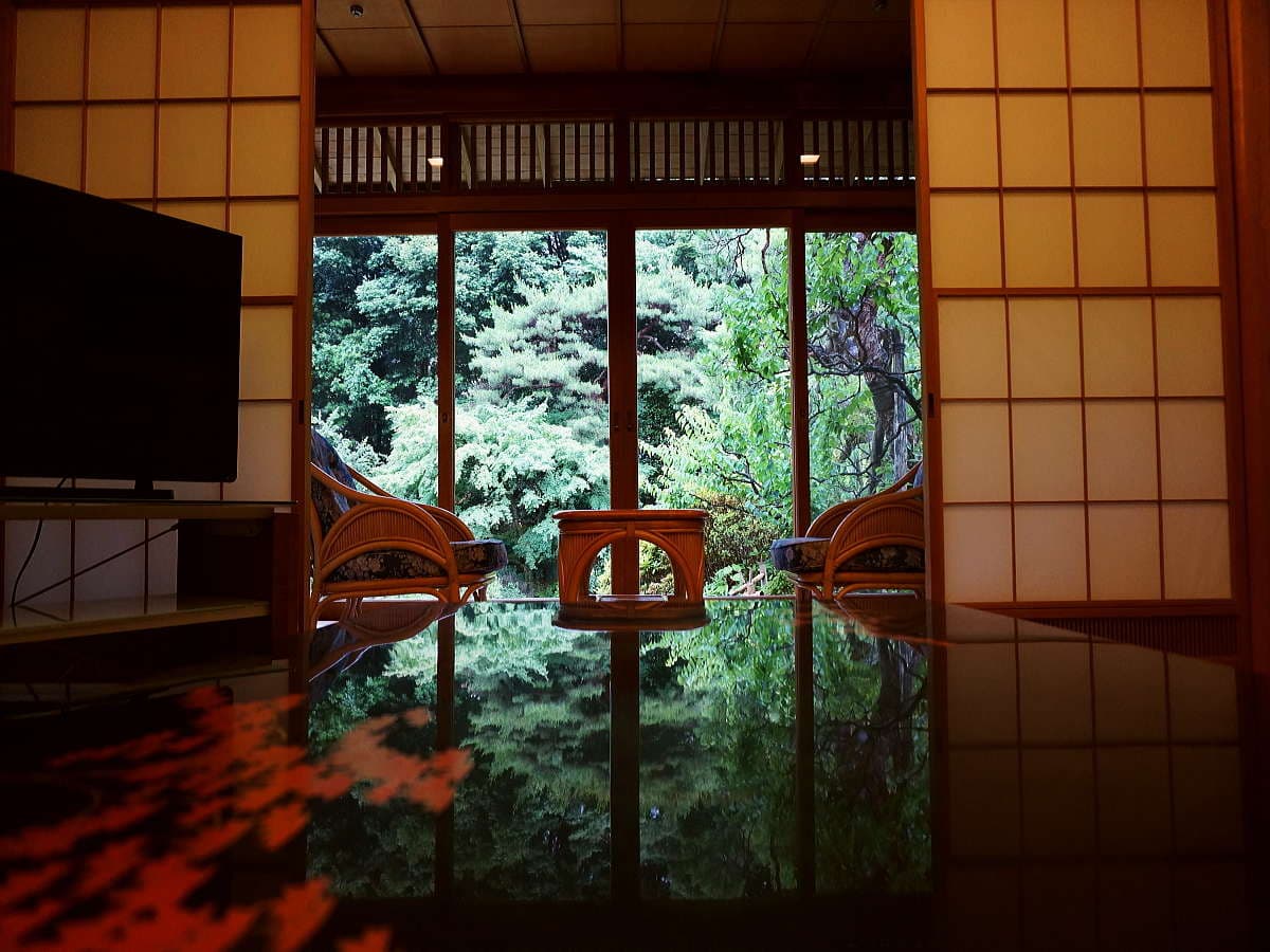 Guest room sitting alcove with rattan chairs framing a lush green garden view at Atami Koarashitei