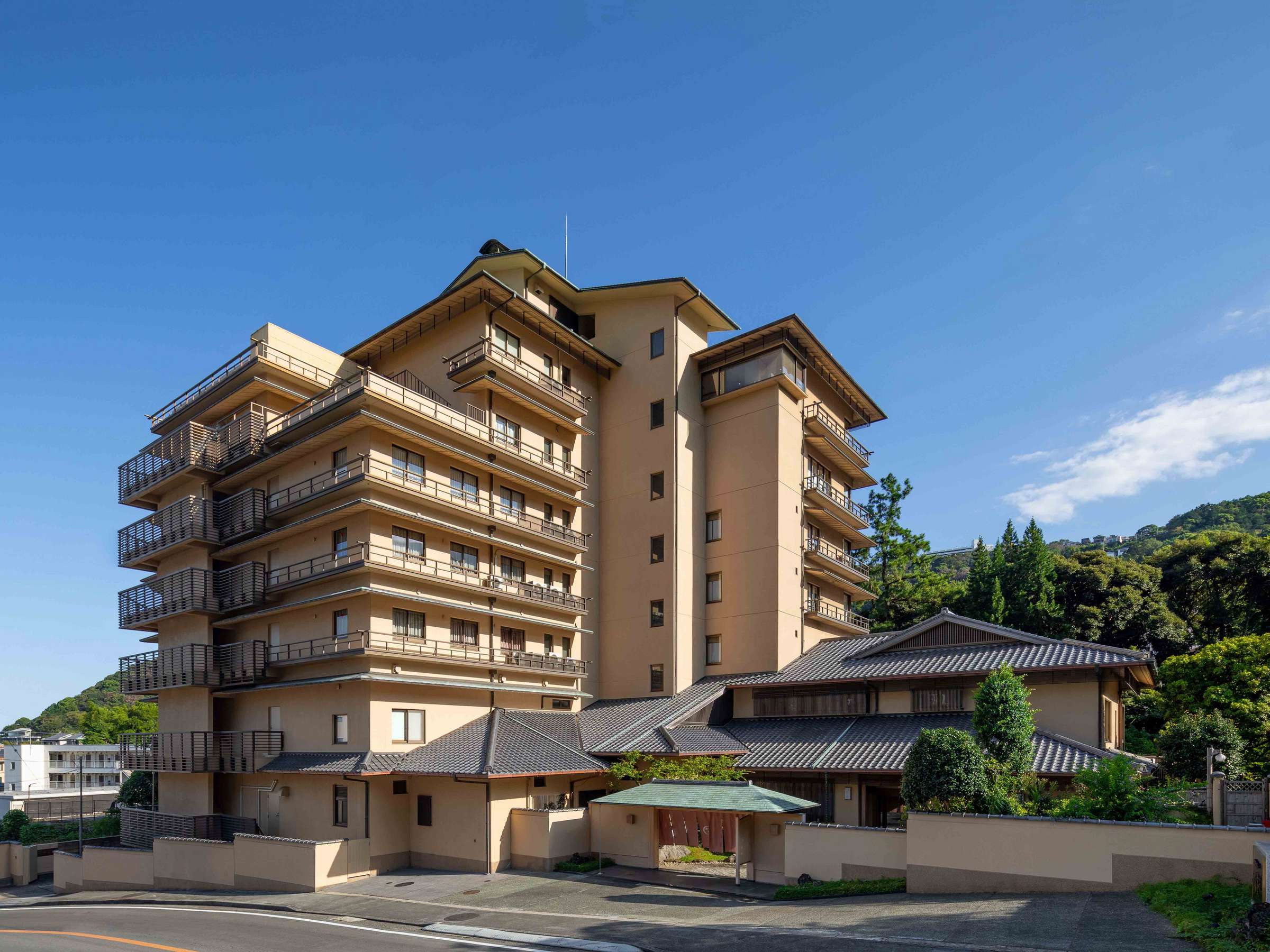 Full daytime exterior of Atami Koarashitei showing the multi-story guest wing and tiled-roof teahouse against blue sky