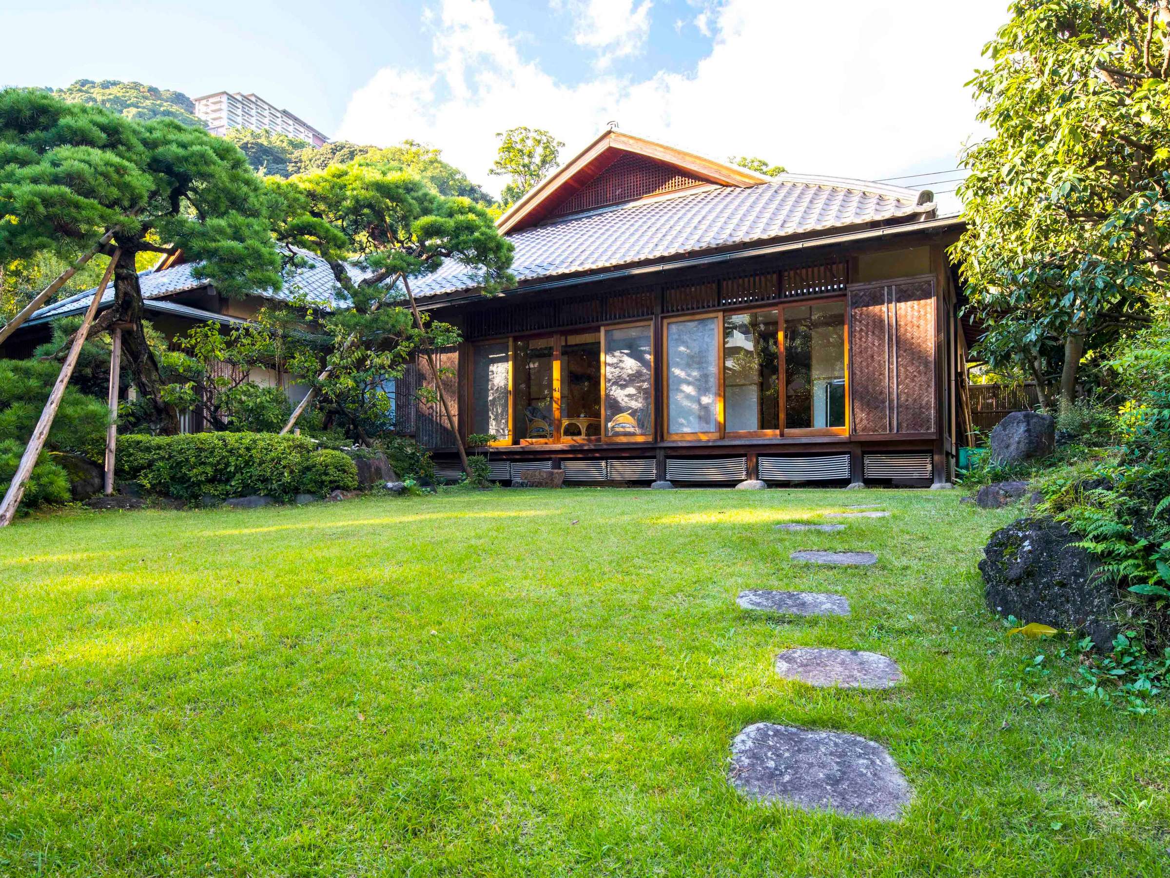 Sukiya-style detached building with stepping stones across a manicured lawn garden at Atami Koarashitei