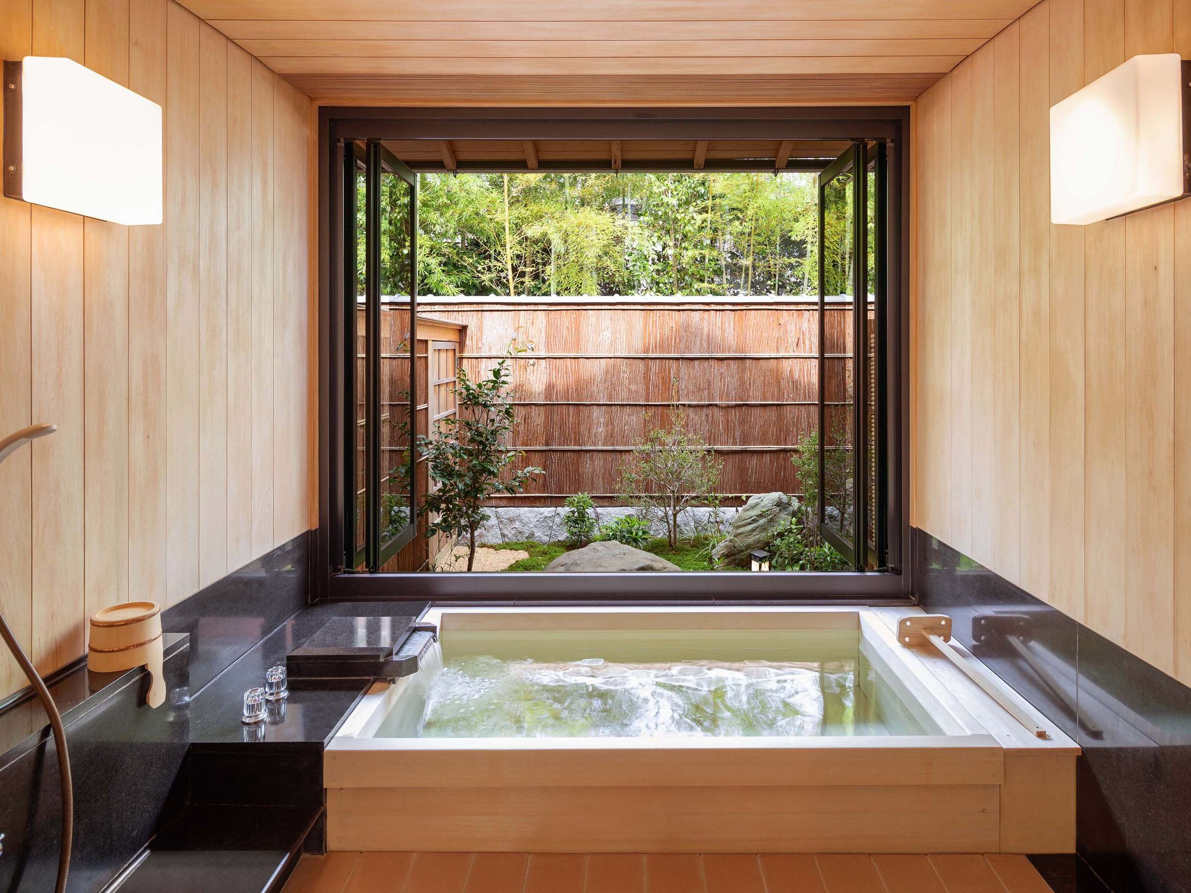 Private hinoki cypress bath with a garden view through a window and bamboo fence at Atami Koarashitei
