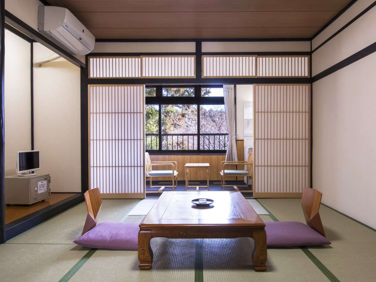 Symmetrical tatami guest room at Nikko Tokanso with a carved wooden table and an enclosed veranda looking out to forest