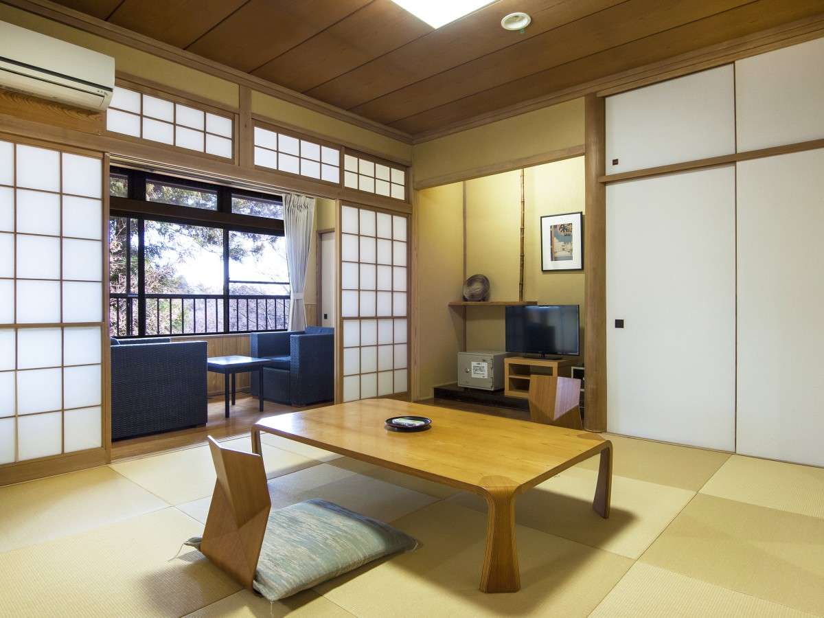 Spacious tatami guest room at Nikko Tokanso with tokonoma alcove and shoji screens opening to a forest-view enclosed veranda