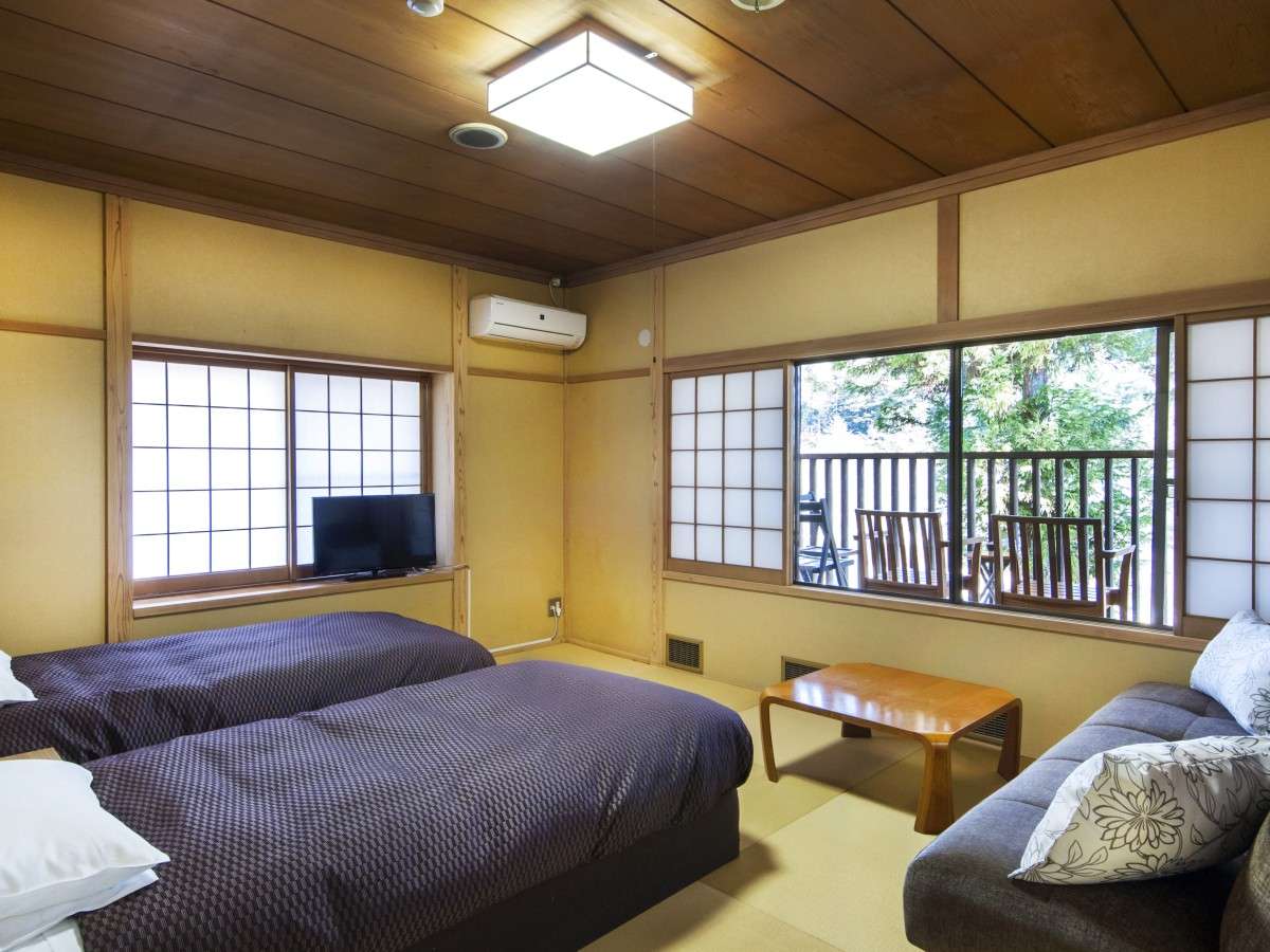 Bright tatami room at Nikko Tokanso with two beds, a sofa and large windows opening onto a wooden balcony in the trees