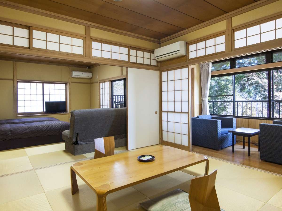 Roomy tatami suite at Nikko Tokanso with twin beds, sofa seating and a sunroom veranda overlooking green woodland
