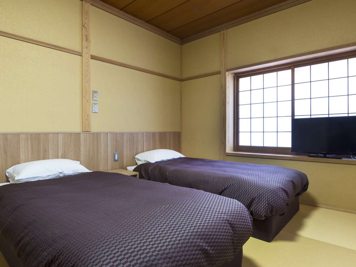 Twin beds set on tatami flooring in a wood-trimmed guest room at Nikko Tokanso with a shoji lattice window