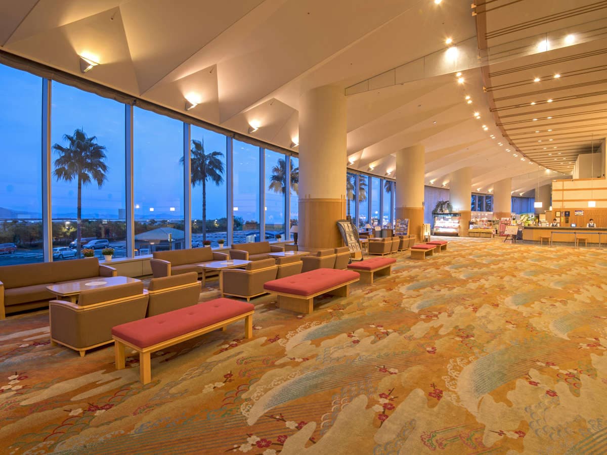 Spacious hotel lobby lounge with armchairs, palm trees and sea view at dusk