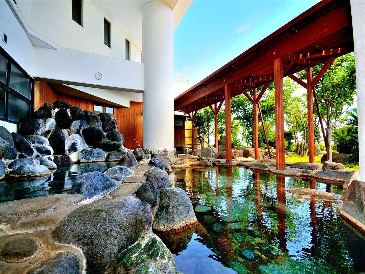 Outdoor rock garden onsen bath beside a wooden pavilion and palms at Hotel Katara, Atagawa Onsen, Izu
