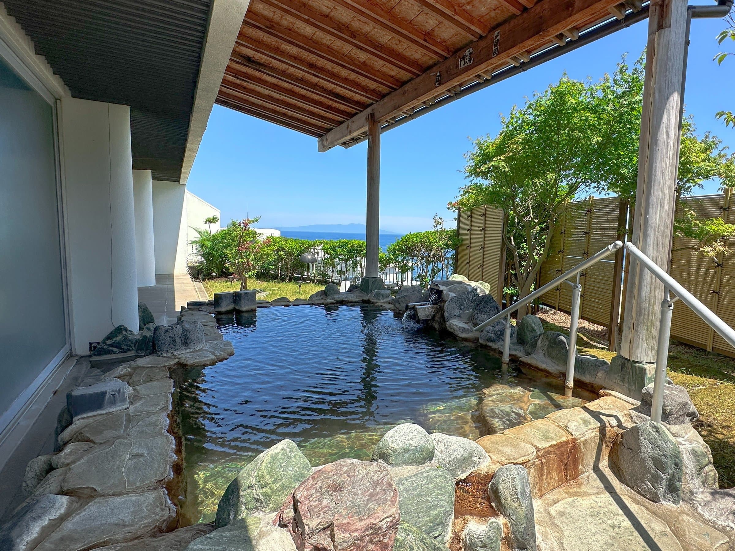 Open-air communal rotenburo bath framed by rocks and greenery with a sea view, Atagawa Onsen Hotel Katara