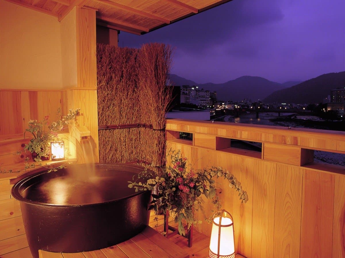 Private cypress tub on a wooden balcony at dusk with steam and river-town views, Yamagataya, Gero Onsen